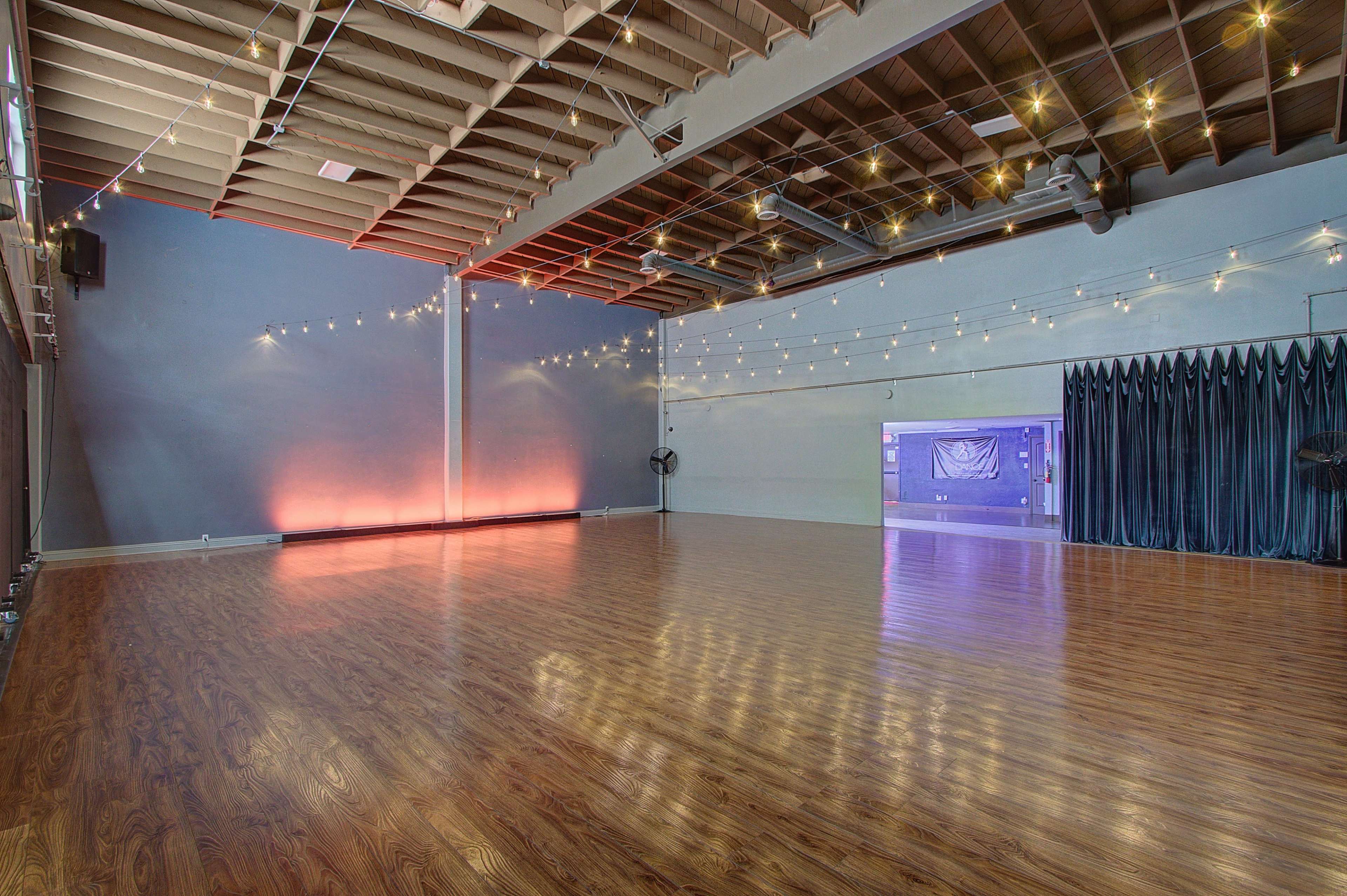 A spacious studio with polished wooden floors, soft lighting, and a curtain-covered stage area.