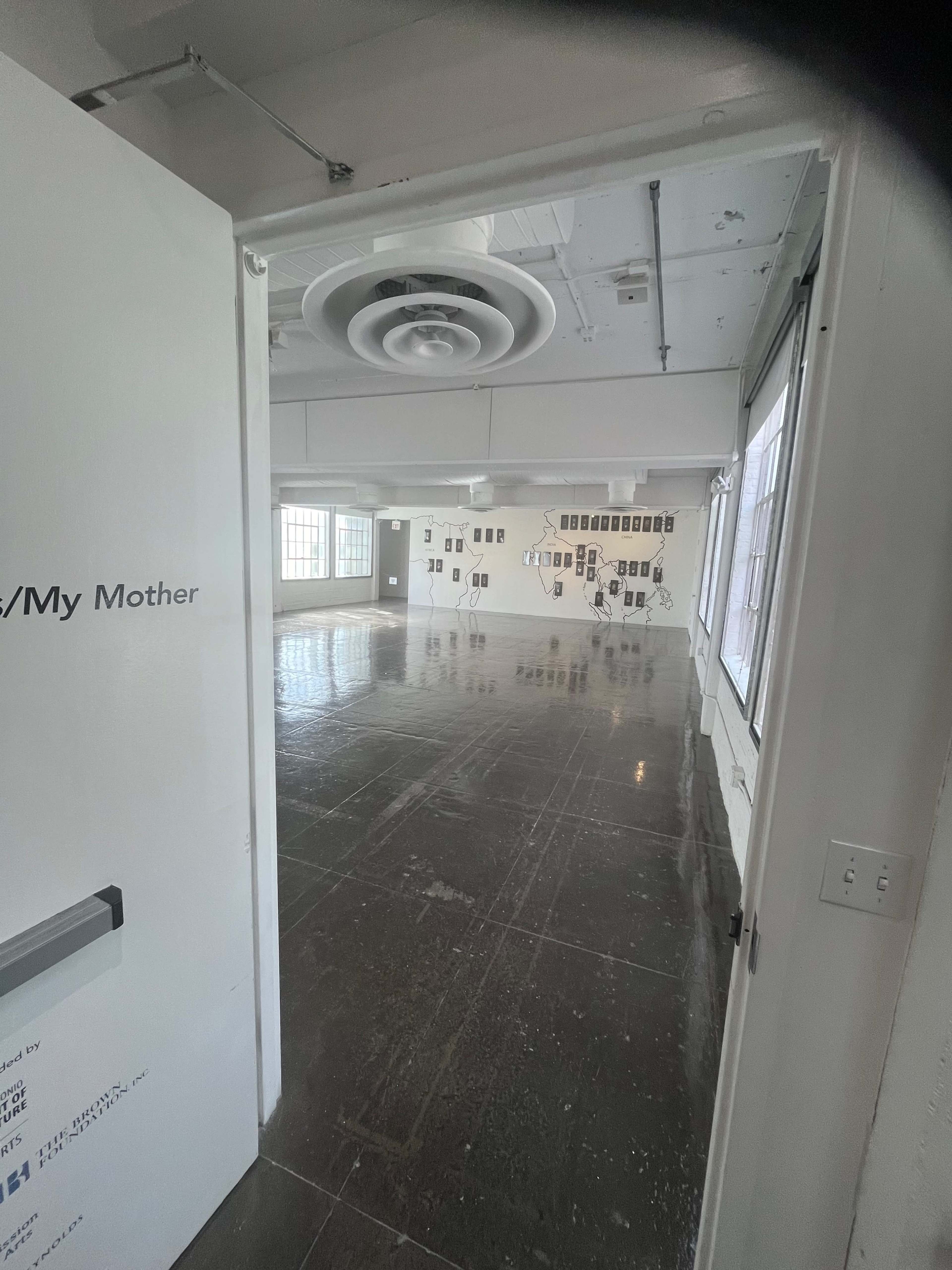 A door opens to a spacious, empty room with polished concrete floors and photographs displayed on the walls.