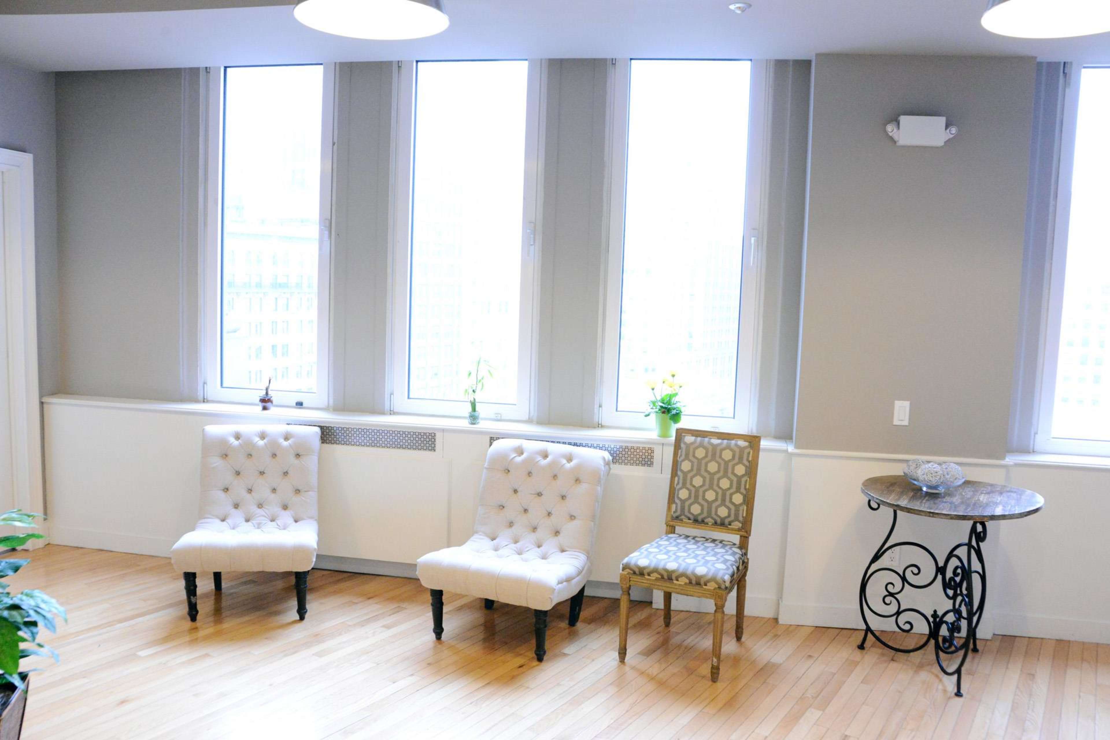 A room with three chairs and a round table near large windows.