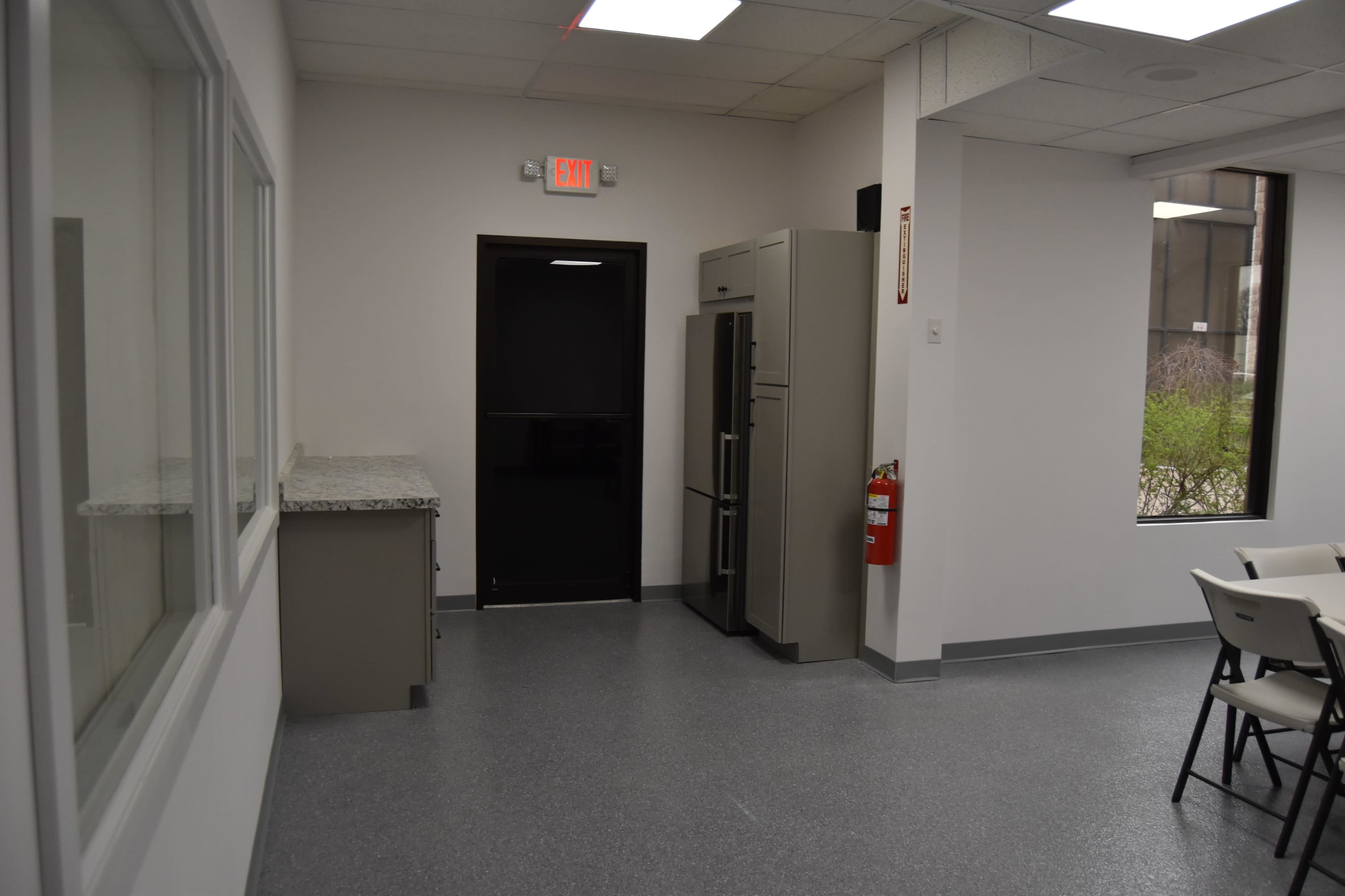 A kitchen area with a countertop, a refrigerator, a black door, and a fire extinguisher mounted on the wall.