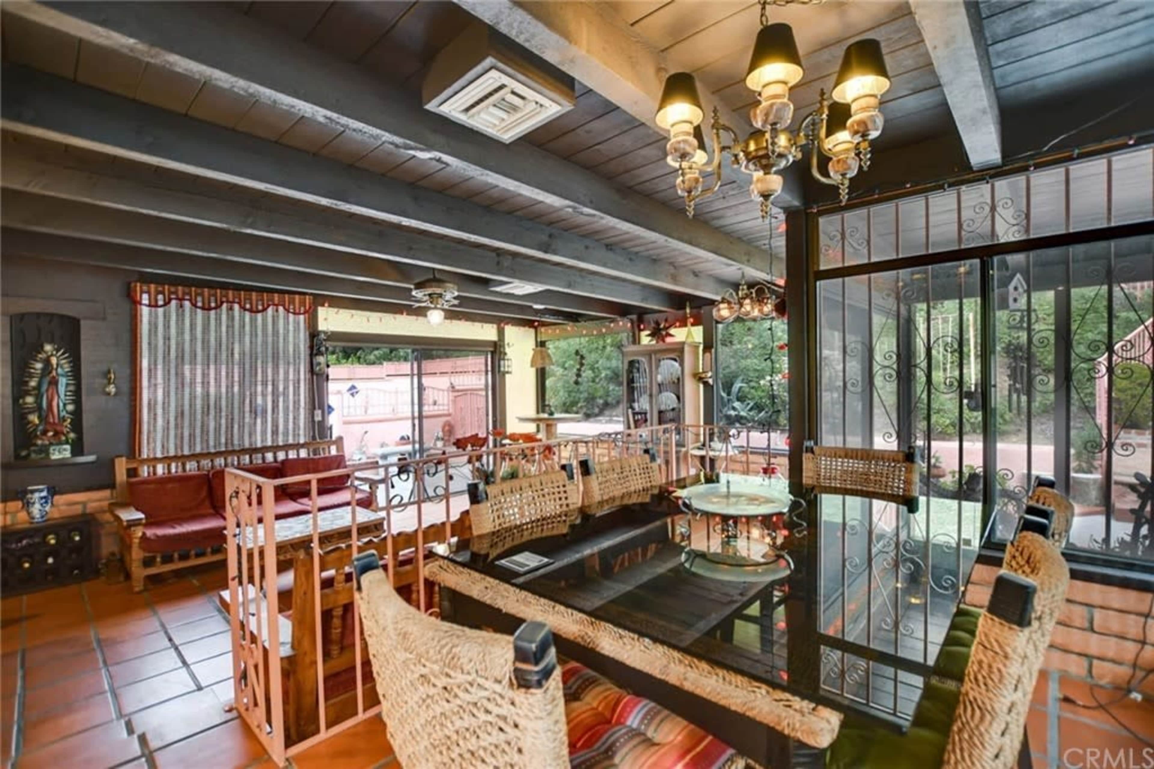 The image shows a sunlit indoor dining area with a table and chairs, large windows overlooking a patio, and decorative elements on the walls.