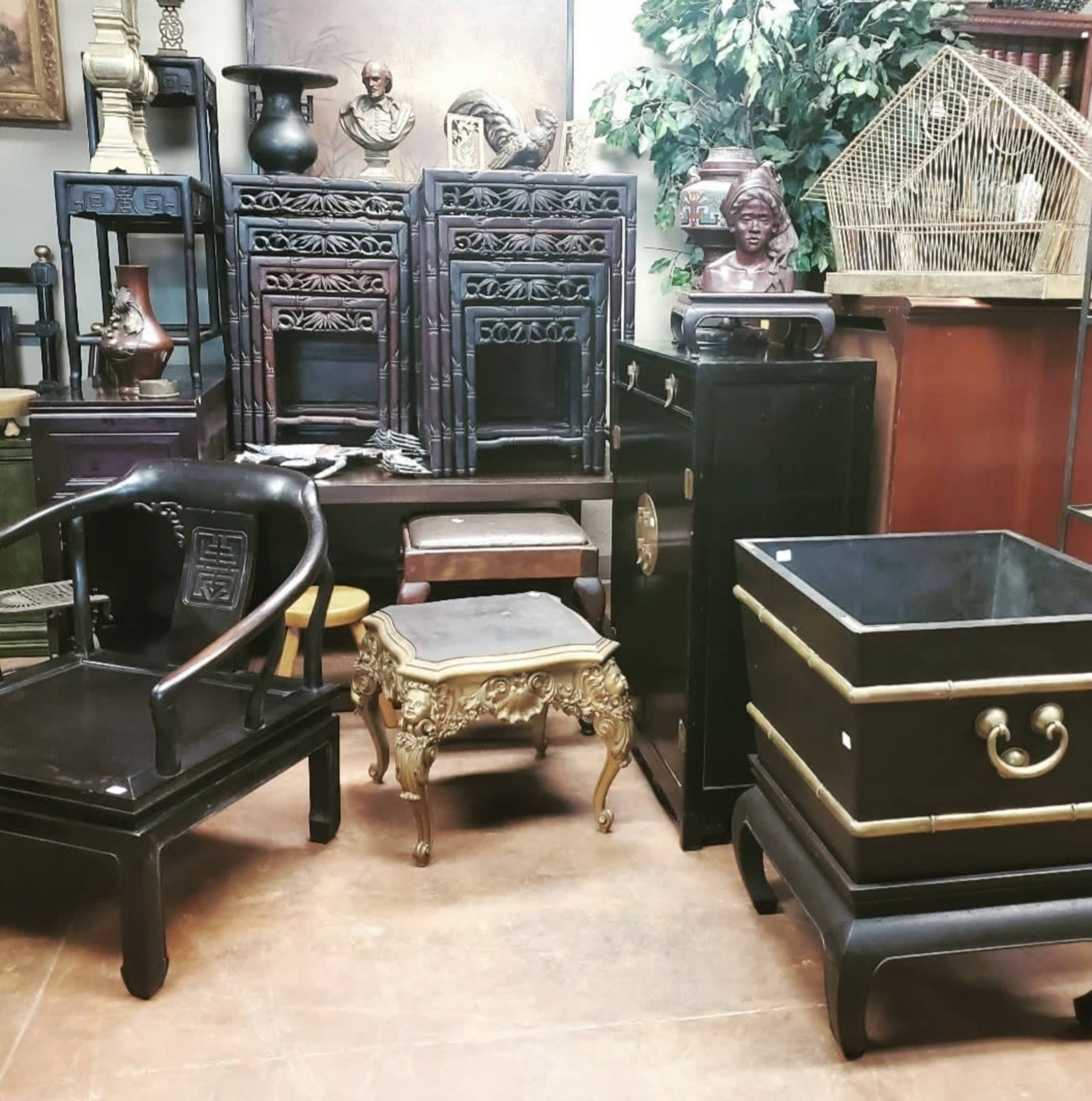 A collection of antique furniture pieces, including black wooden cabinets, a decorative gold-accented table, and a black storage box, arranged in a room with plants and decor.