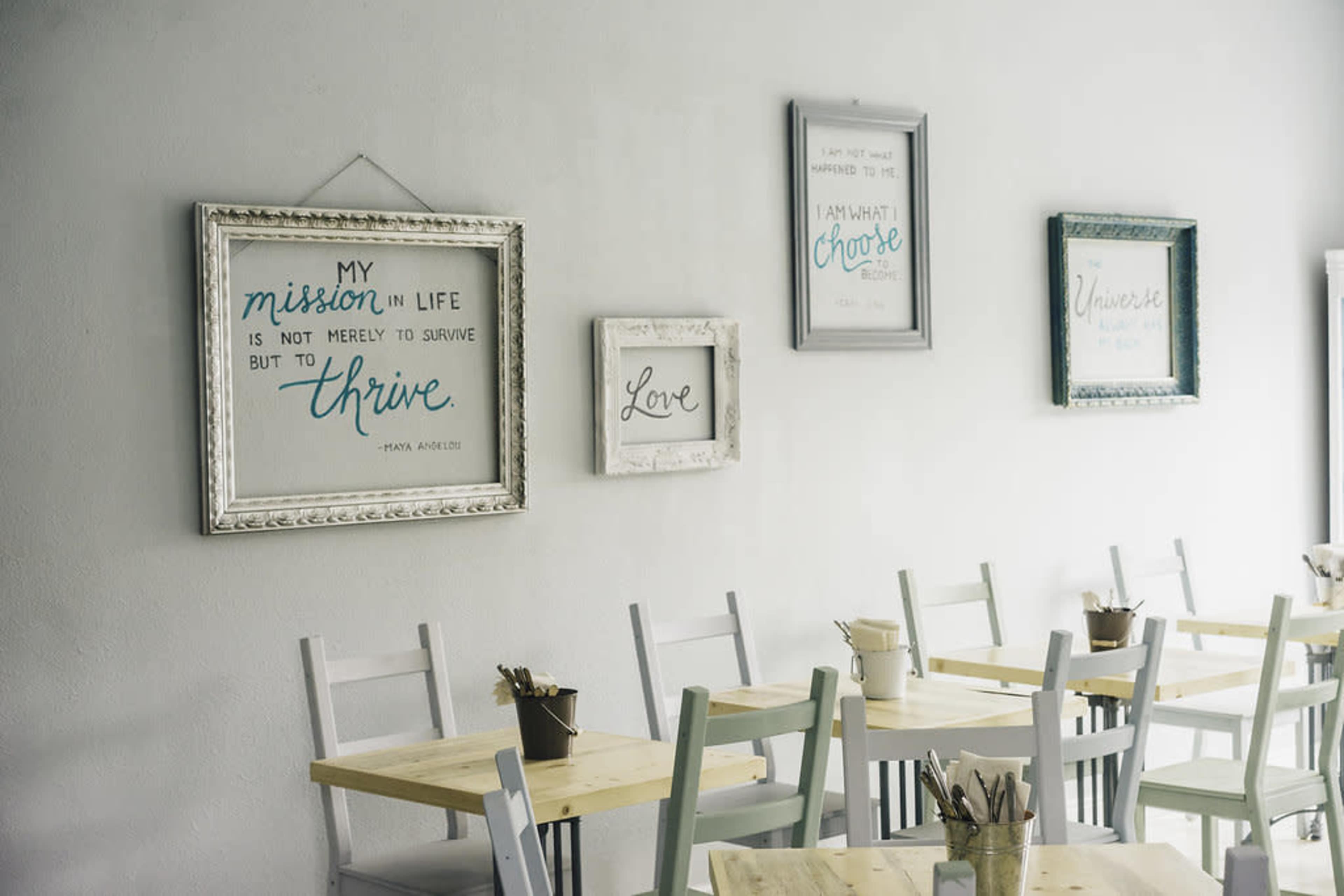 A minimalist café interior with framed inspirational quotes on the walls and wooden tables and chairs arranged neatly.