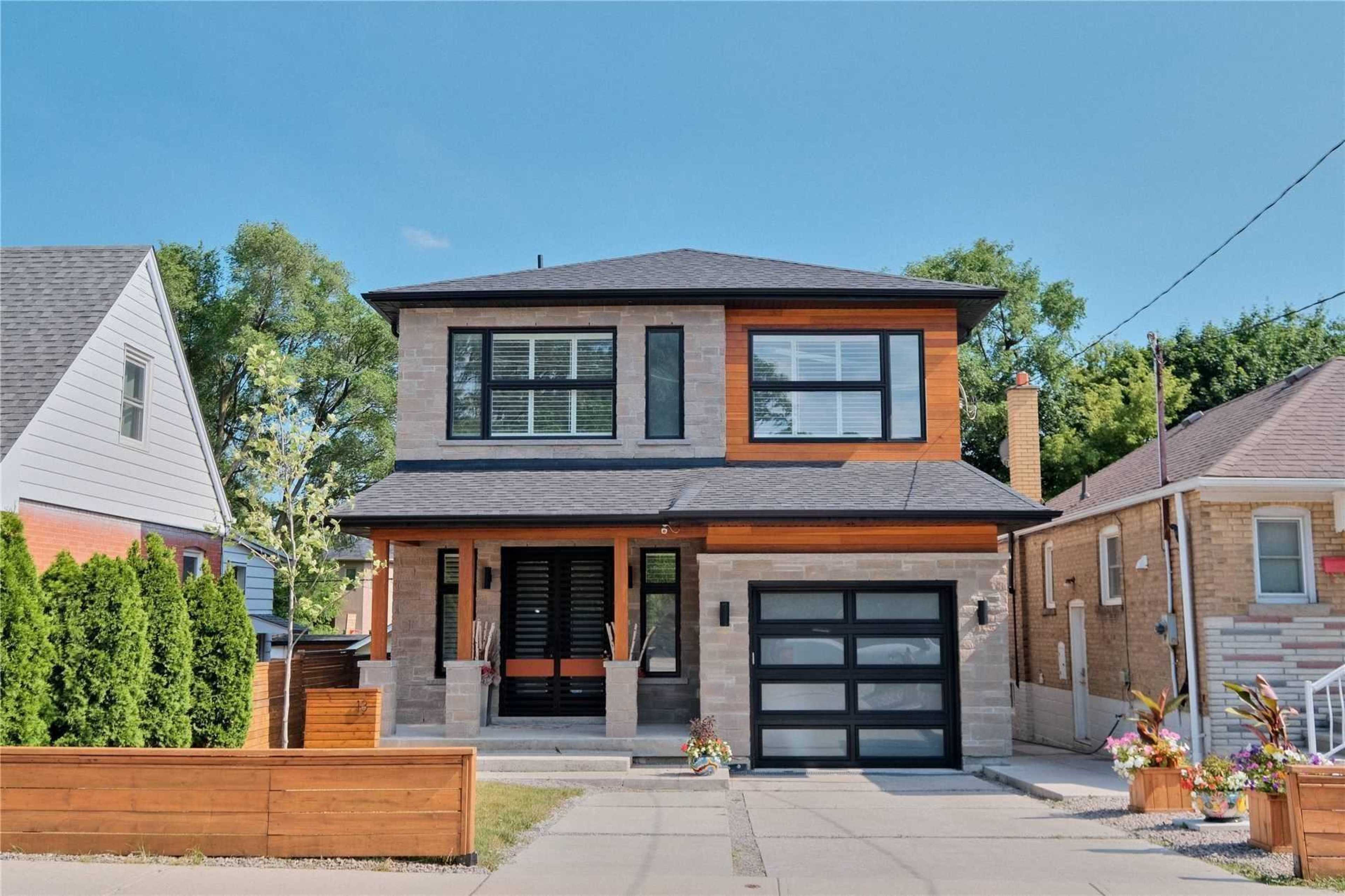A modern two-story house with a mix of stone and wood siding, a black garage door, and landscaped front yard.