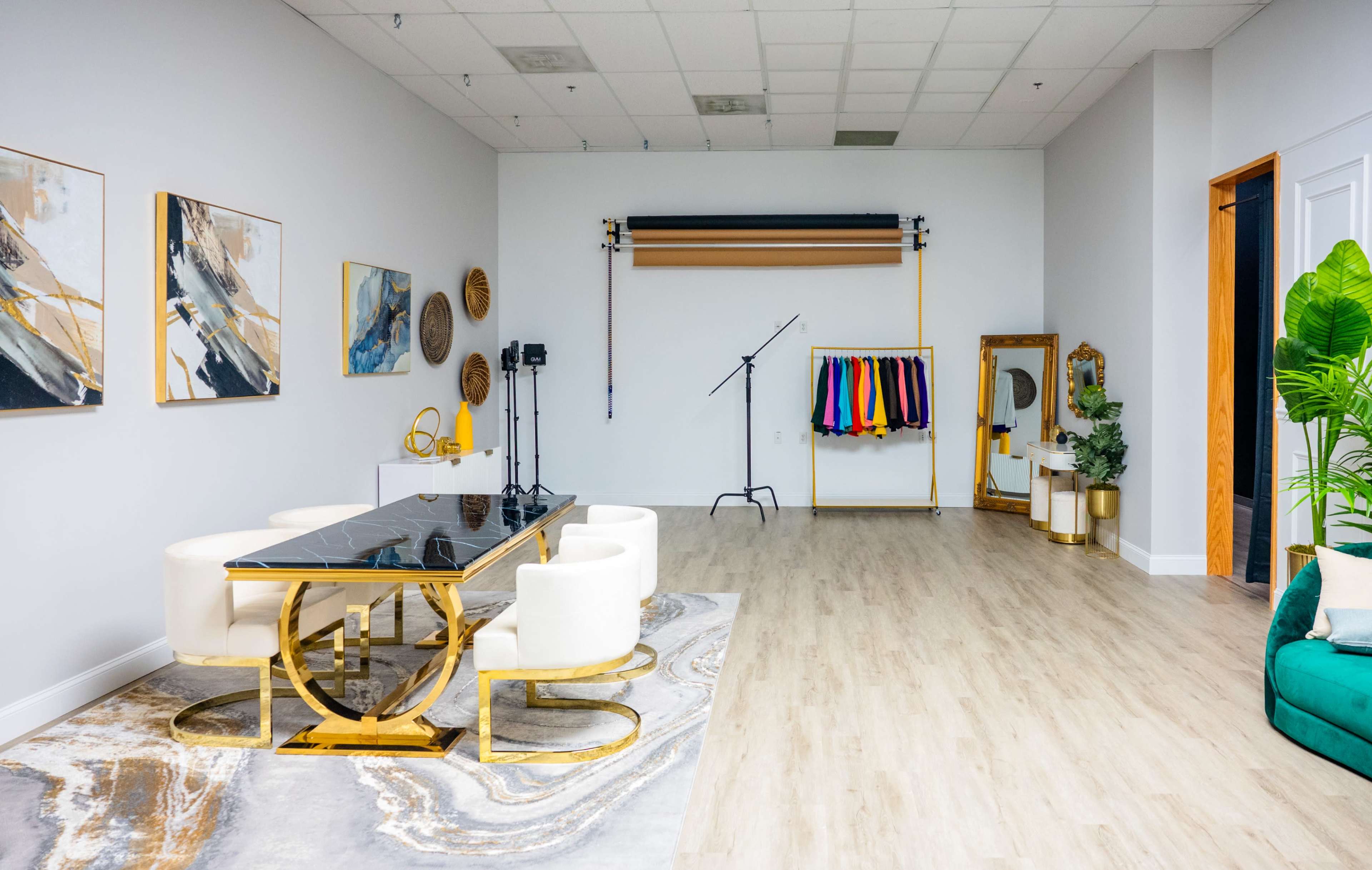 A spacious interior with a modern dining table, white chairs, colorful fabric drapes hanging on a rack, and decorative artwork on the walls.
