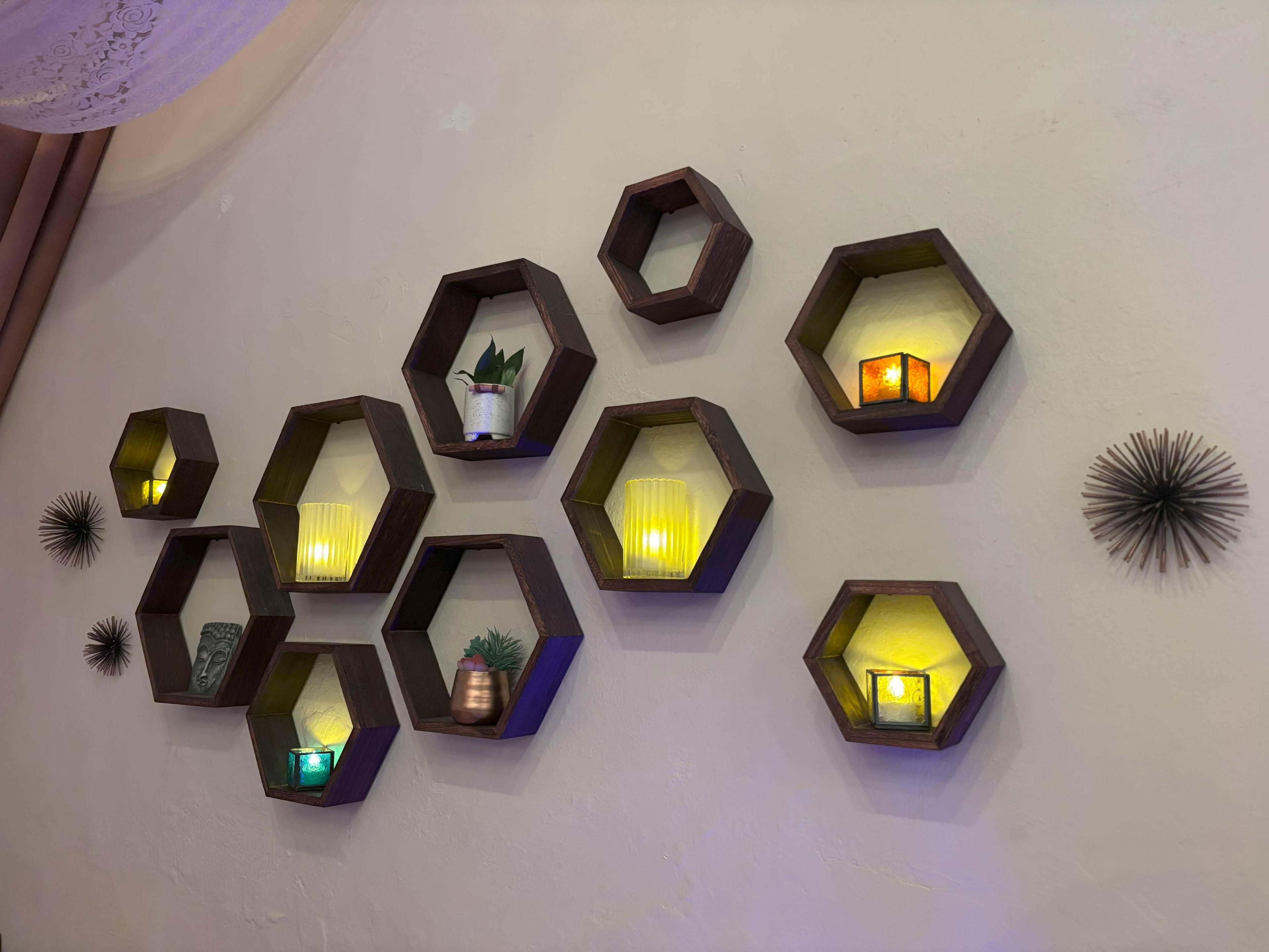 A wall displays a series of hexagonal shelves arranged in a pattern, holding various plants and candles that emit a warm glow.