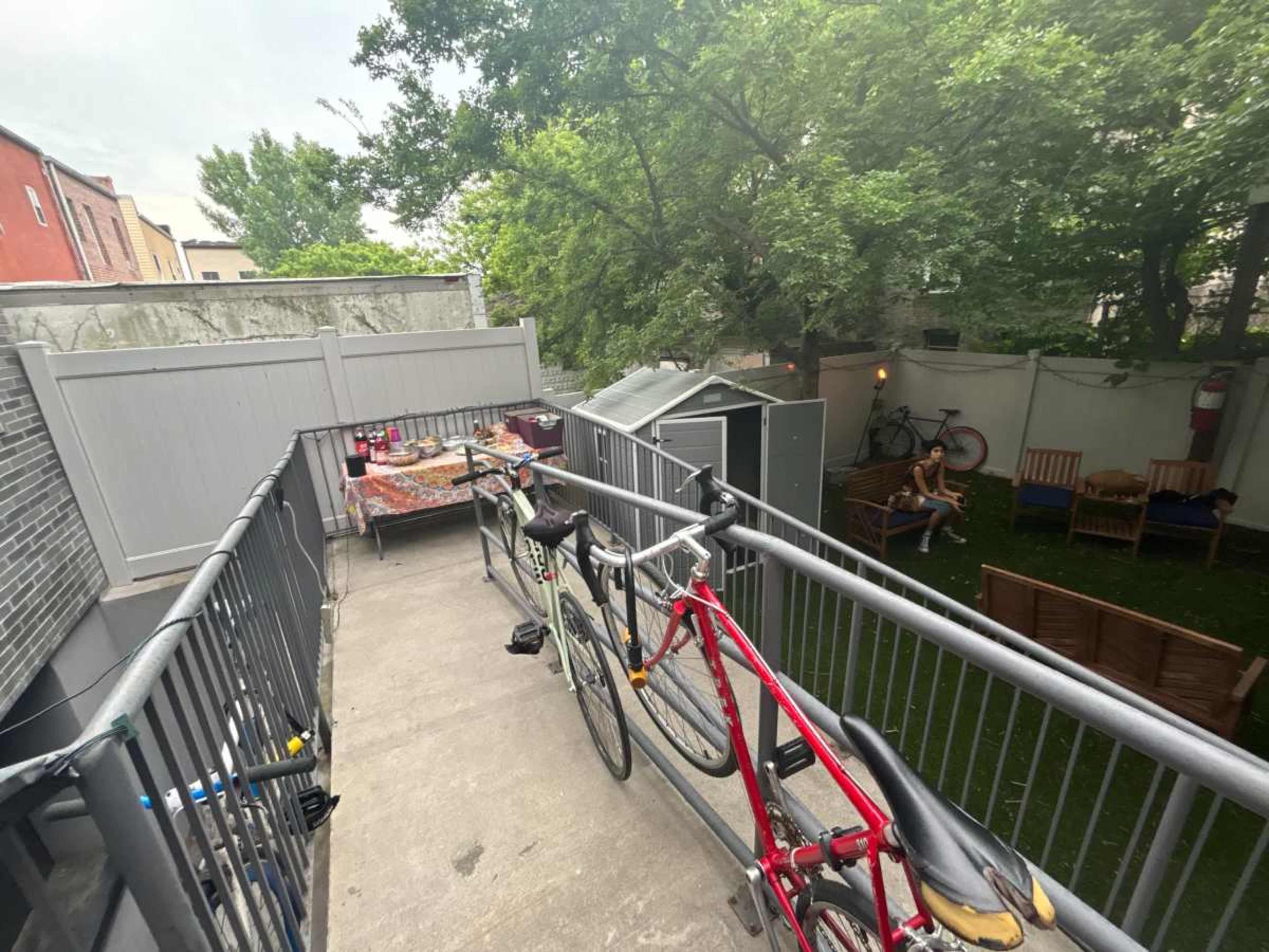 A balcony features two bicycles parked on the railing with a view of a small, grassy yard and seating area below.