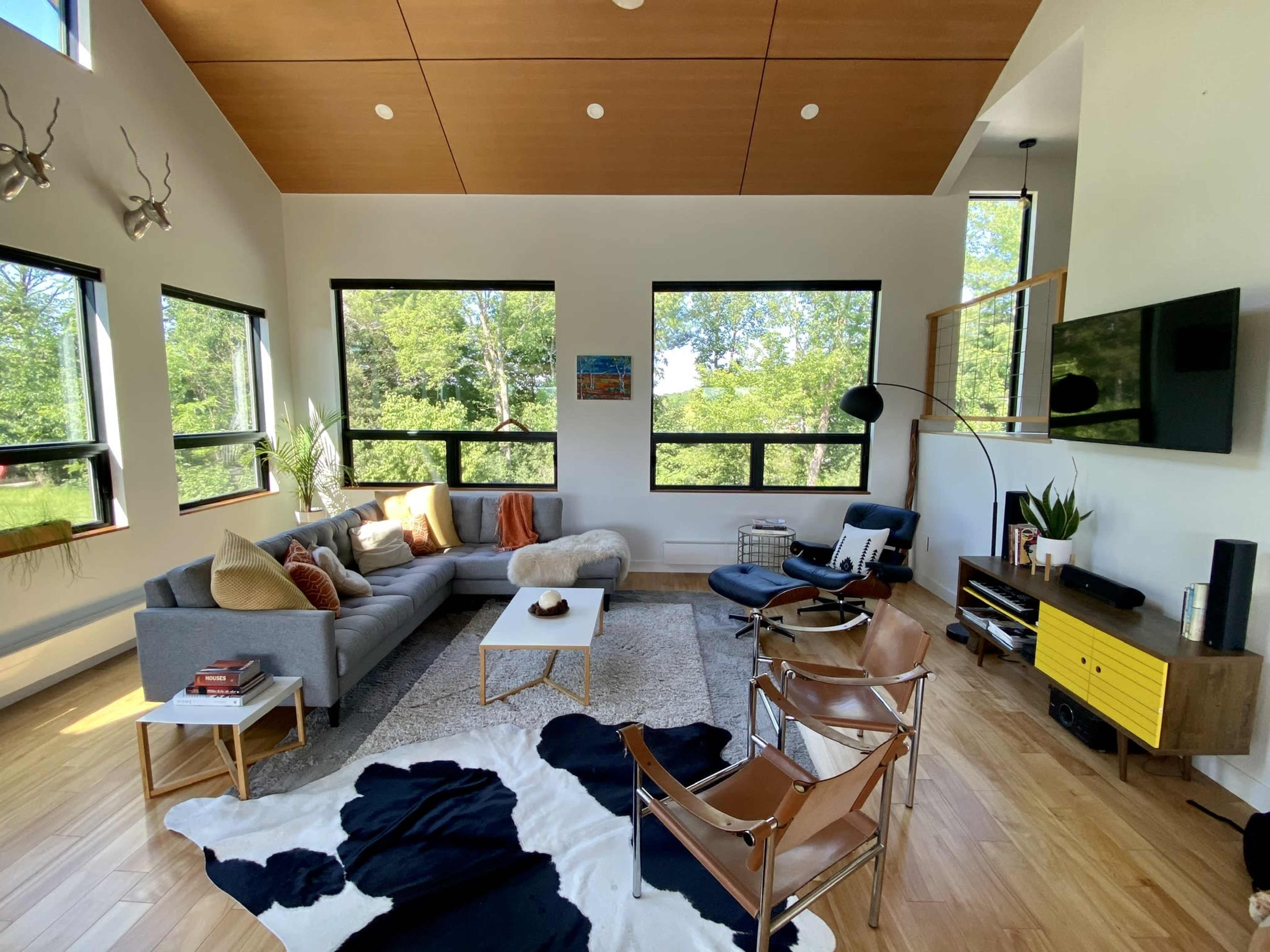 A modern living room with large windows, a gray sectional sofa, a coffee table, and a cowhide rug, complemented by a chair and a yellow side table.