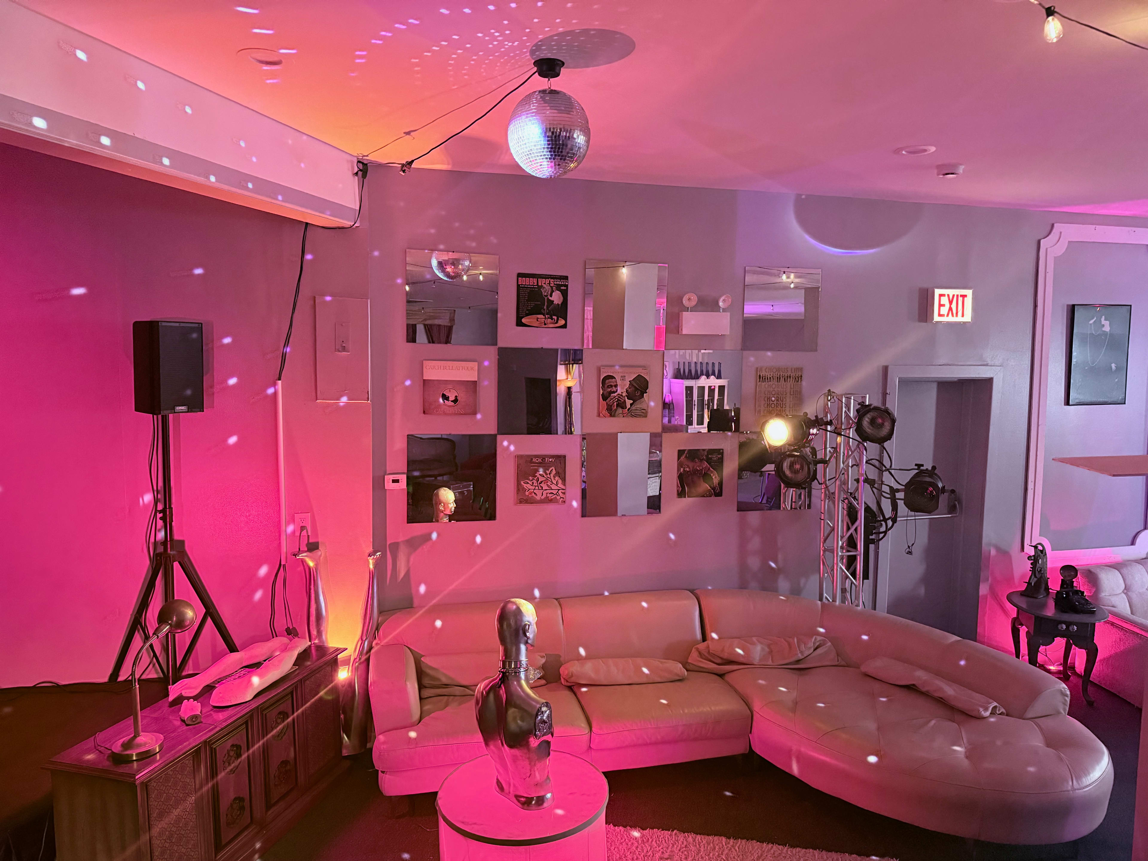 A modern lounge area features a circular sofa, a disco ball reflecting colorful lights, and various decorative mirrors on the walls.