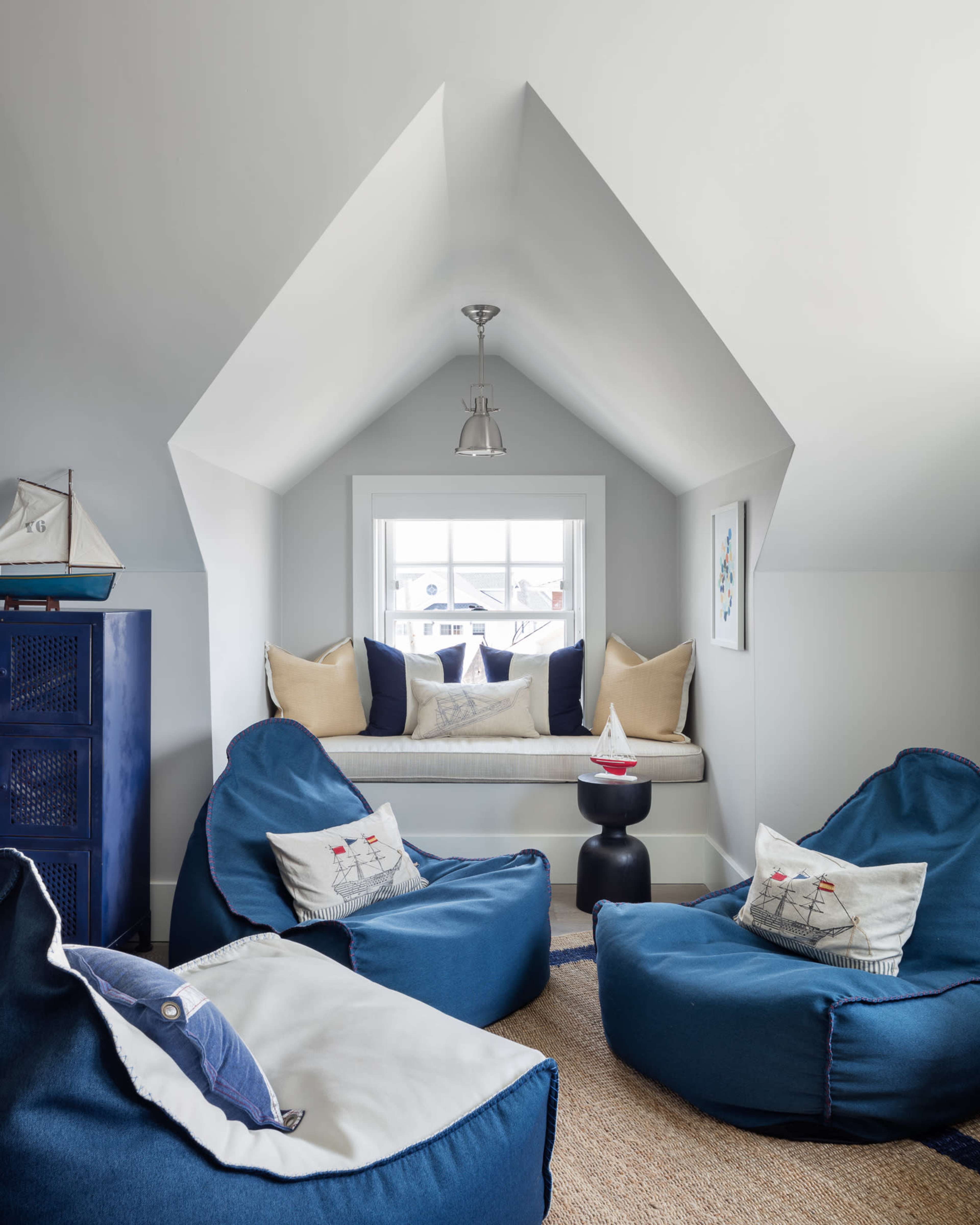A cozy nook with a window seat surrounded by blue bean bag chairs and neutral decor in a room with a sloped ceiling.