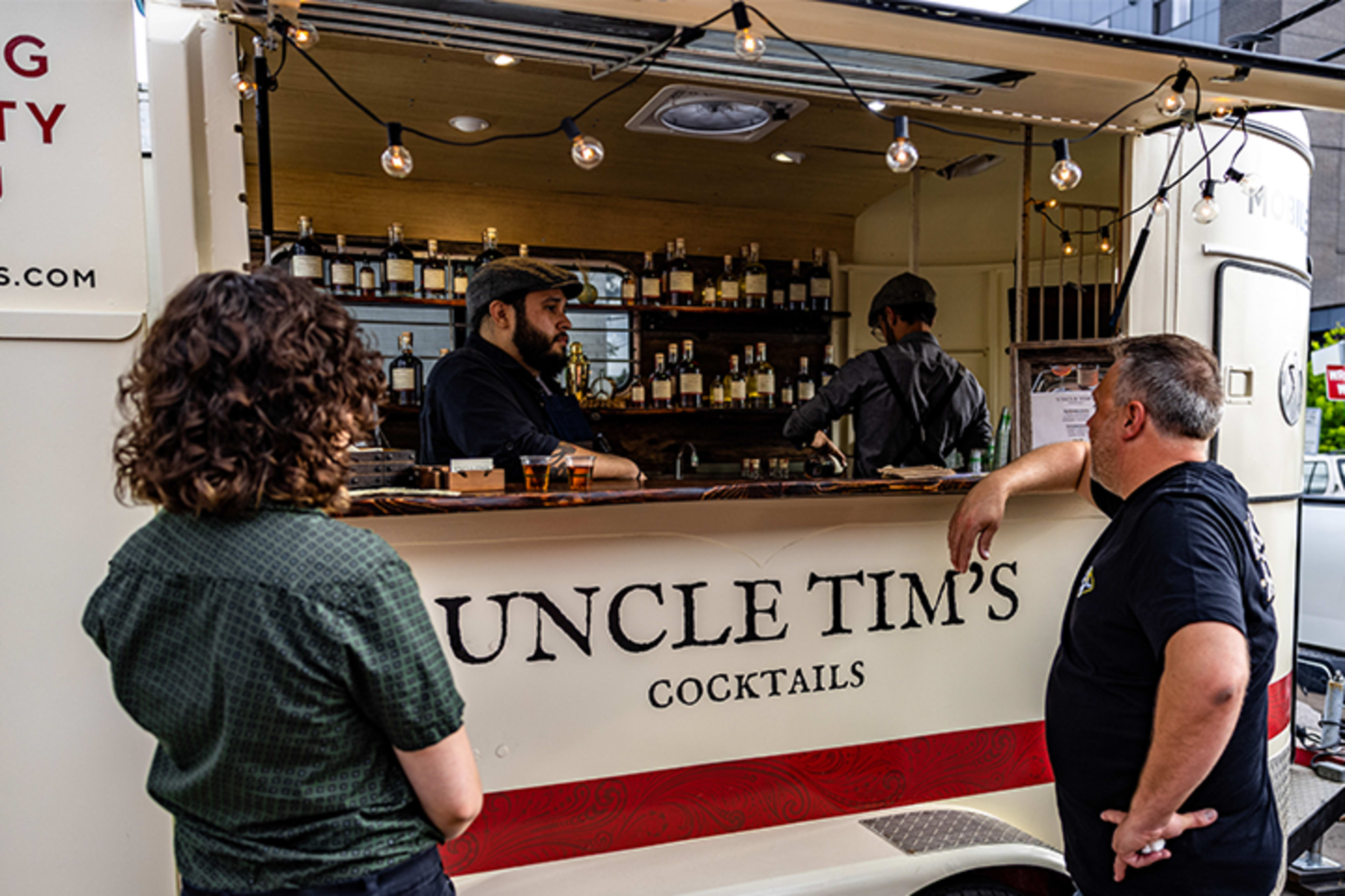 A cocktail truck named "Uncle Tim's" serves drinks to customers at an outdoor event.
