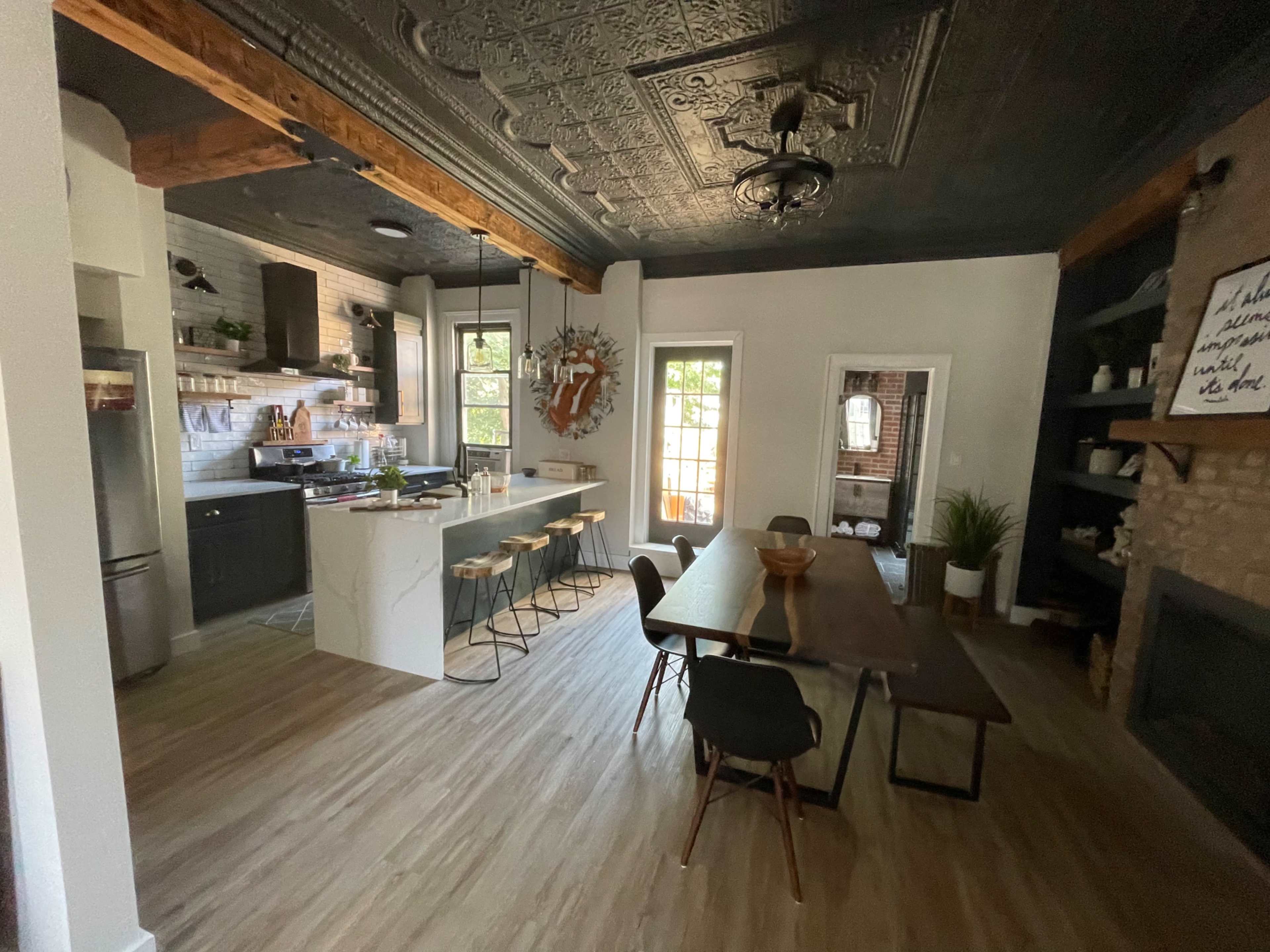 A spacious kitchen and dining area features a modern kitchen island with bar seating, a wooden dining table, and large windows allowing natural light to enter.