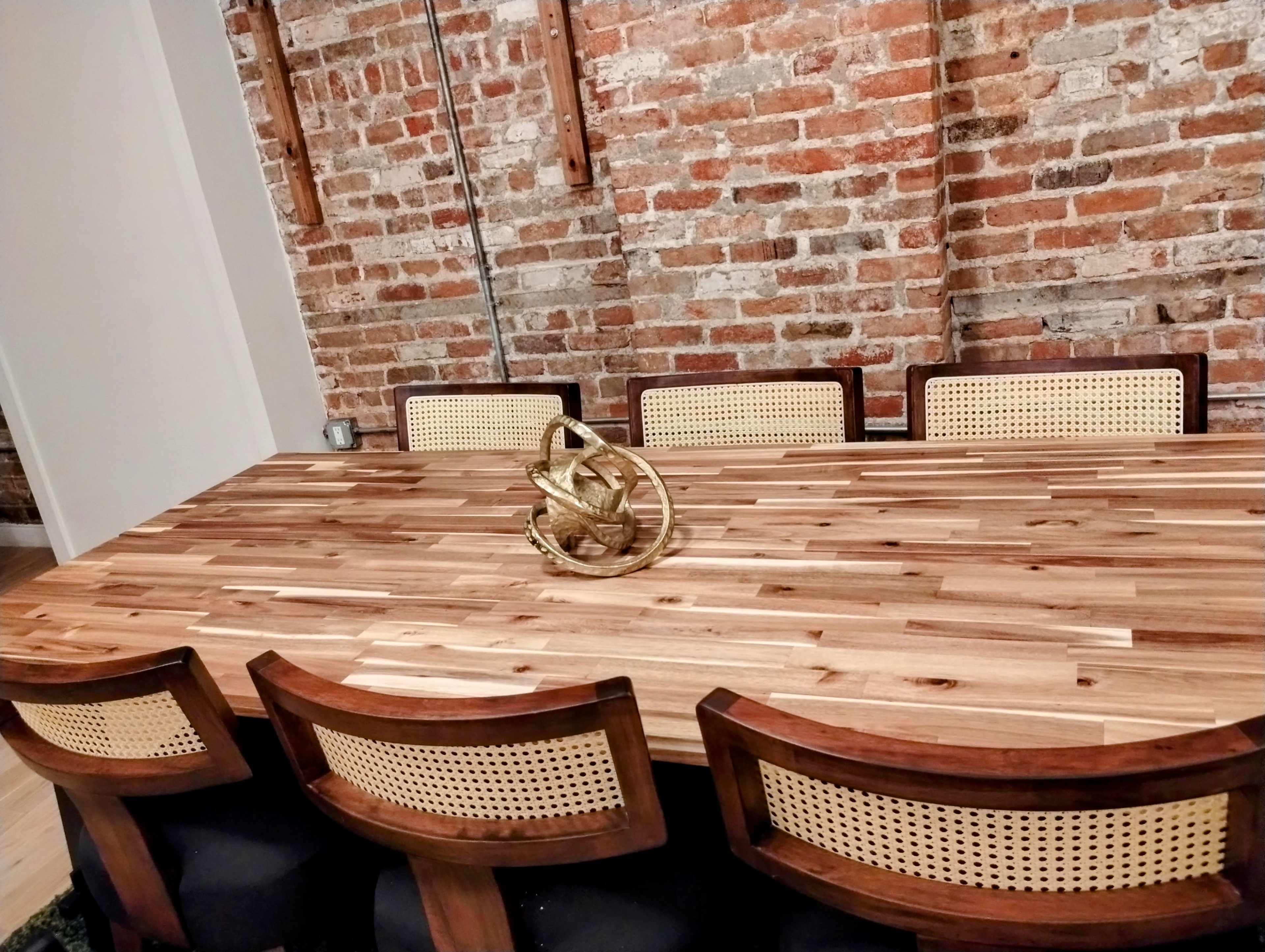A spacious wooden table with a decorative golden sculpture in the center, surrounded by six upholstered chairs, set against a backdrop of exposed brick walls.