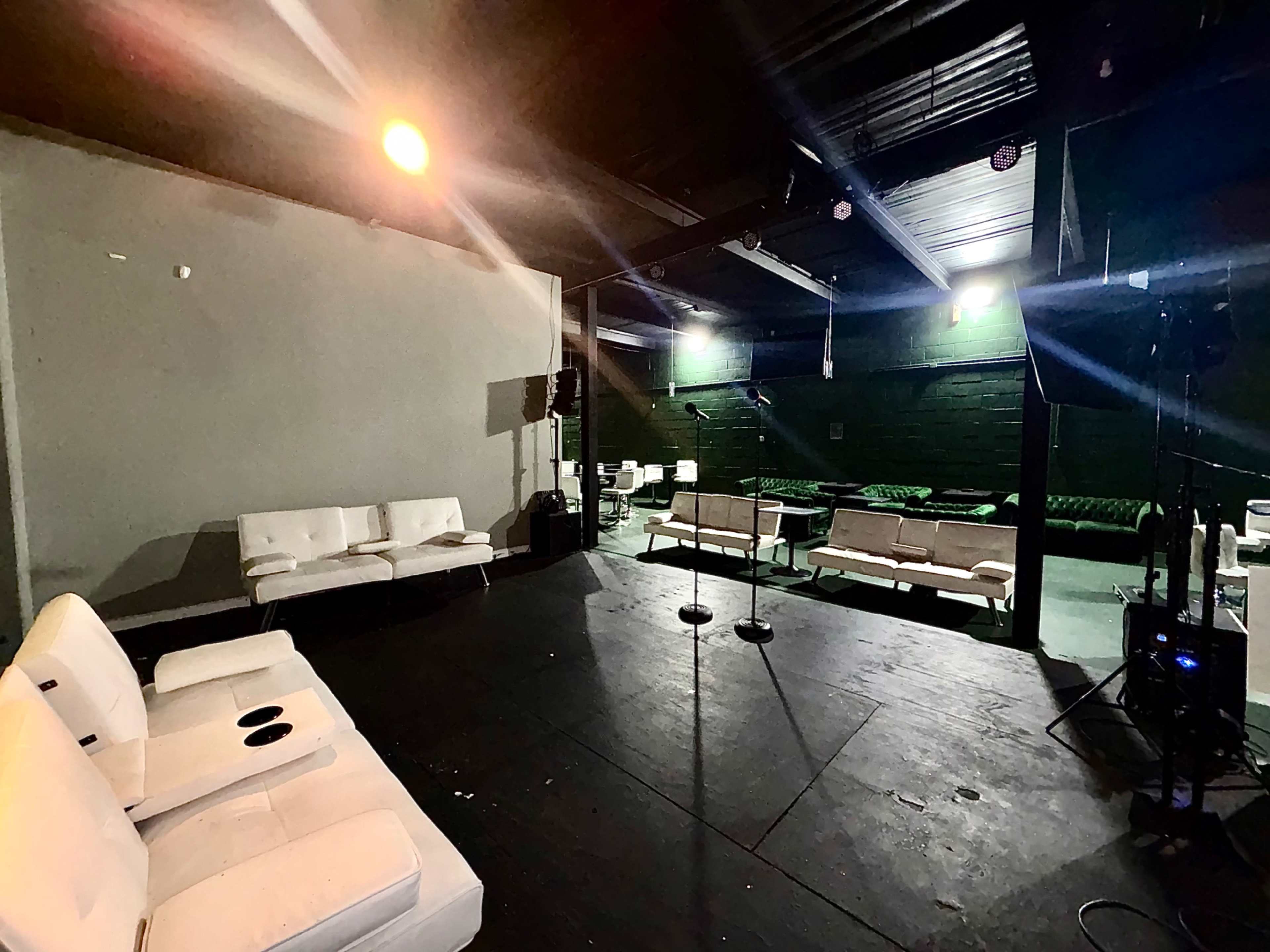 The image shows an empty event space with white couches arranged on a dark floor and a small stage area in the background.