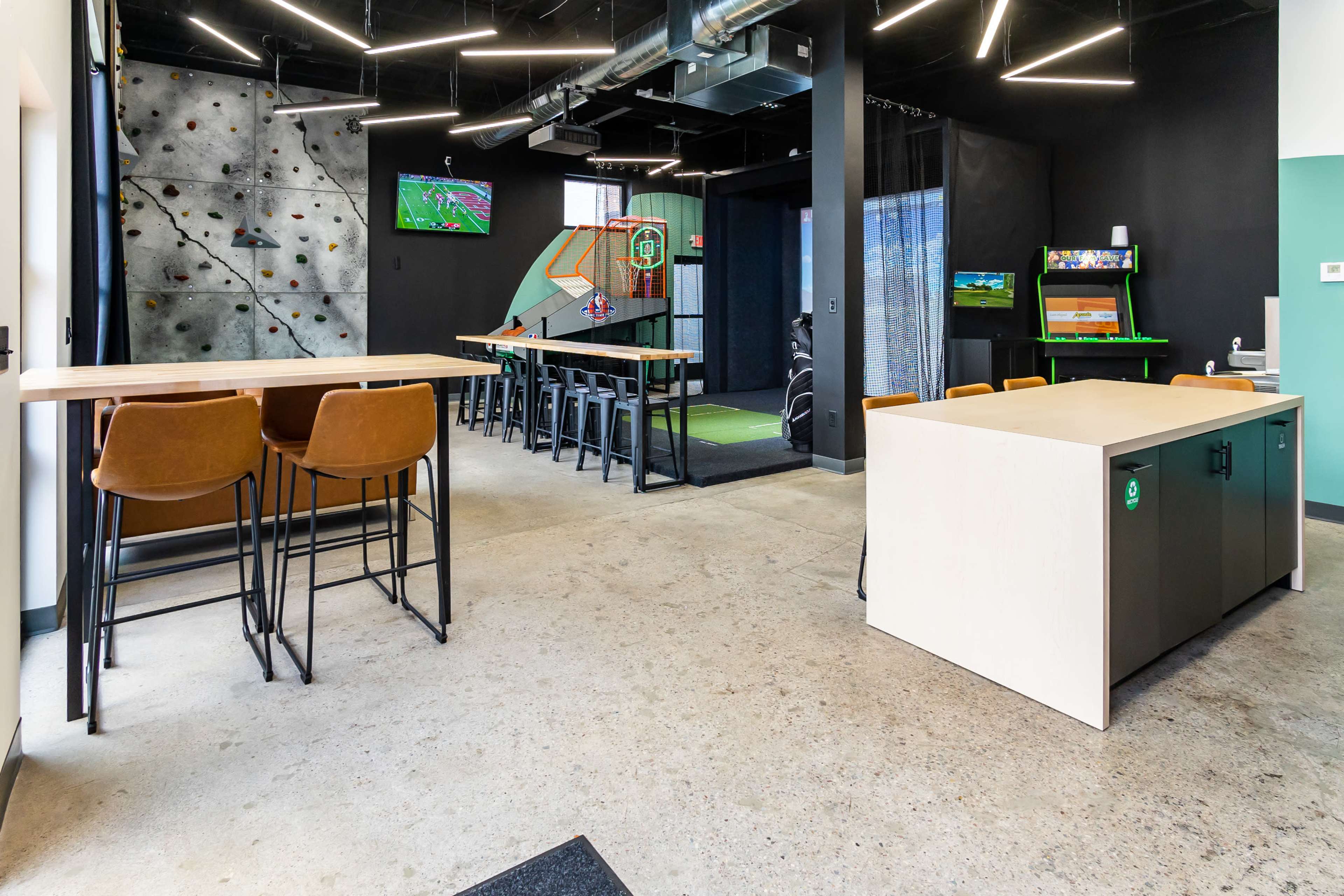 The image shows a modern recreational room with a climbing wall, multiple seating areas, and gaming stations.