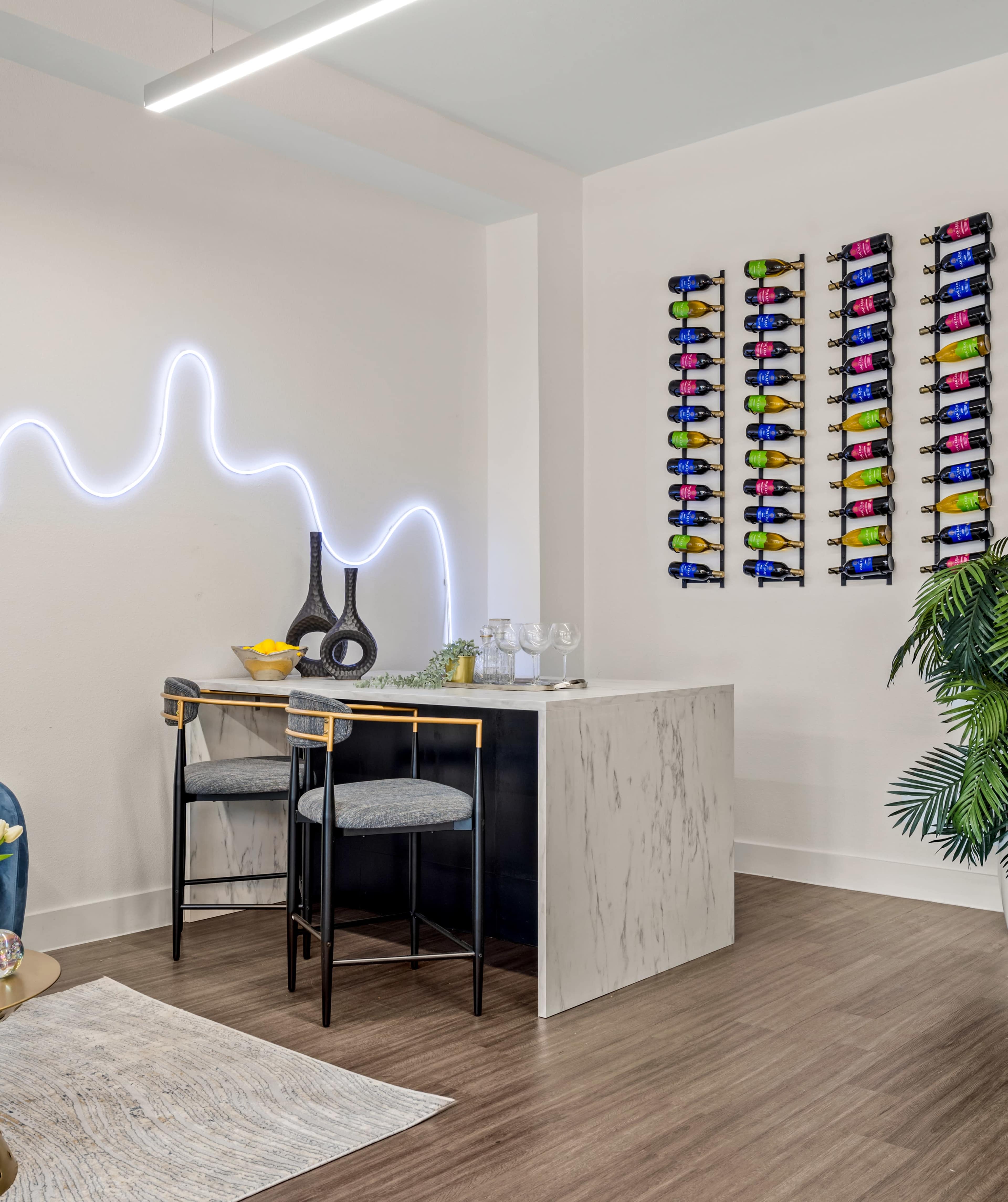 A modern seating area features two black chairs at a marble-top bar with a wine display mounted on the wall behind it.