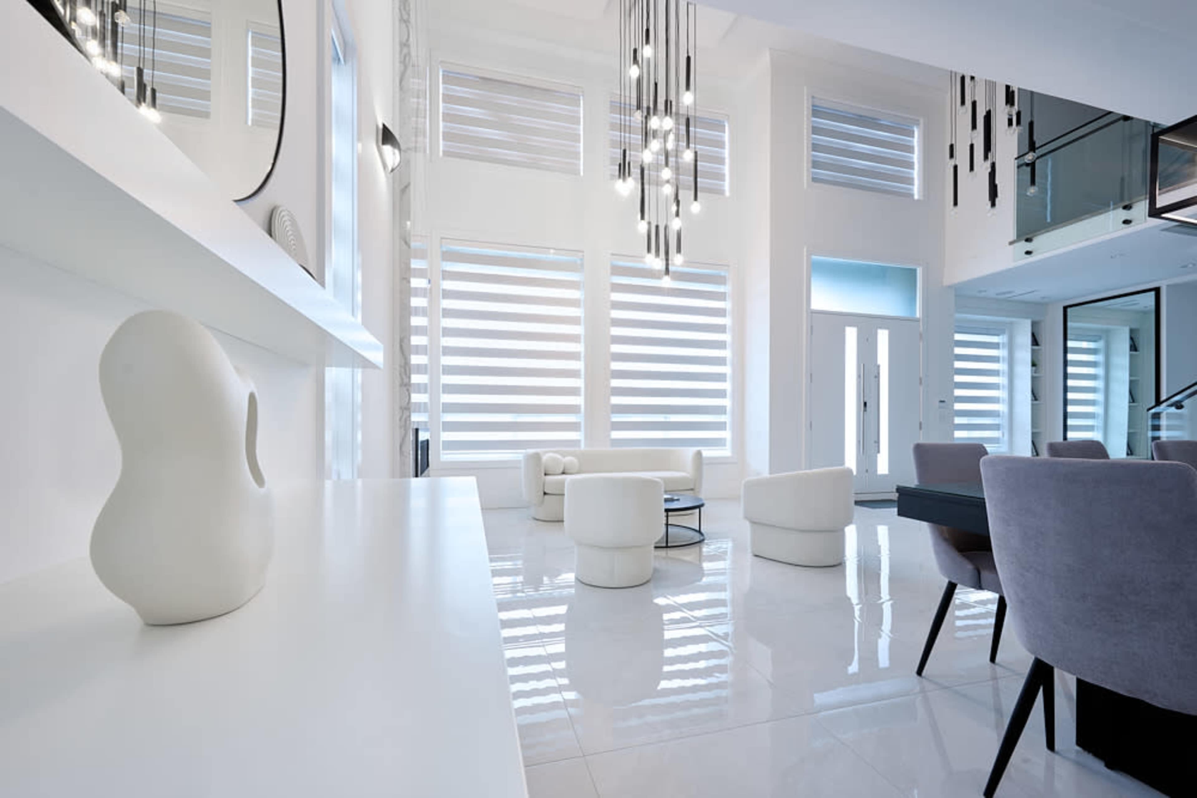 A modern interior space featuring white walls, large windows with shades, minimalist furniture, and polished floors.