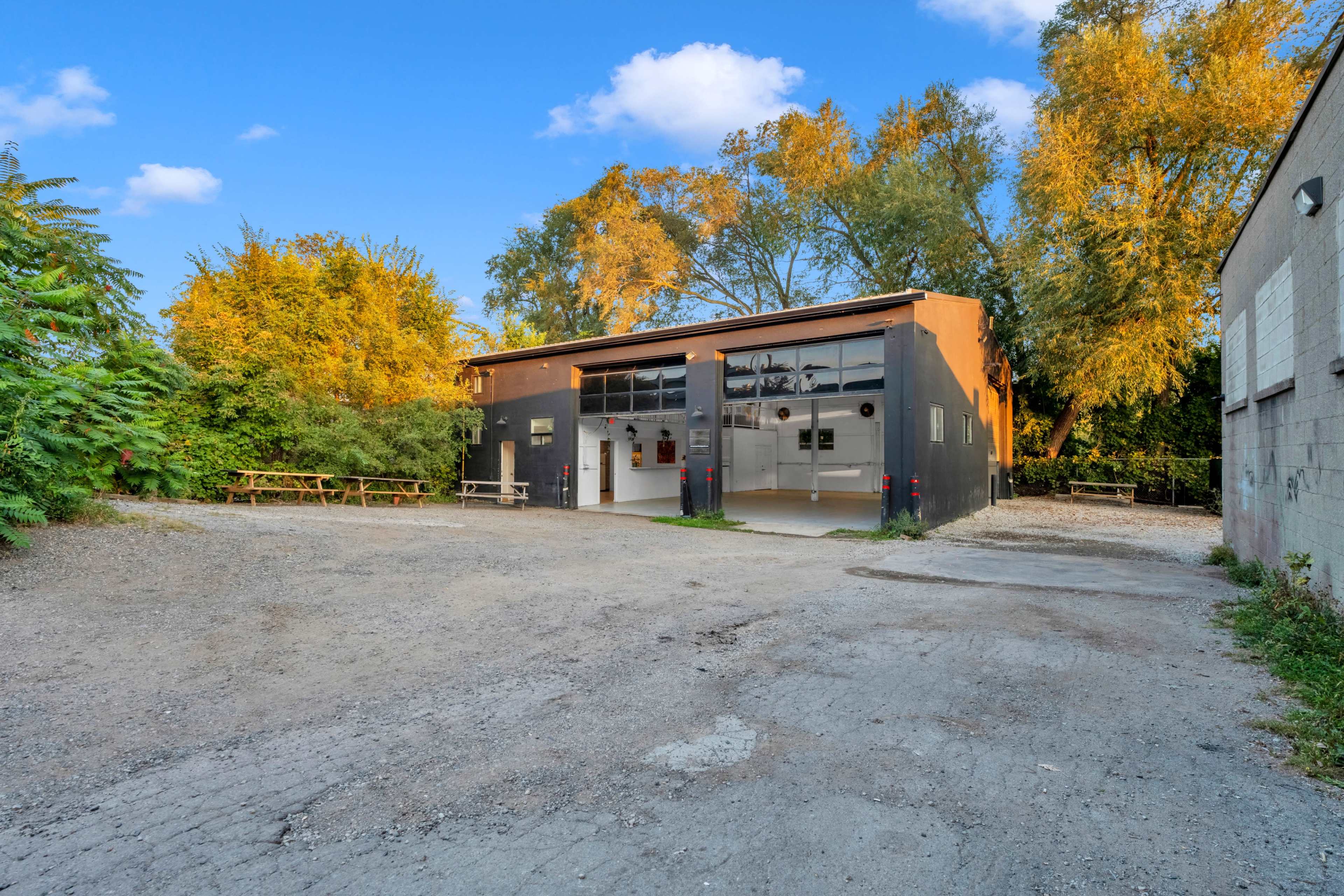 A modern, black building with large windows is set against a backdrop of trees, with a gravel area in front and a few benches visible.