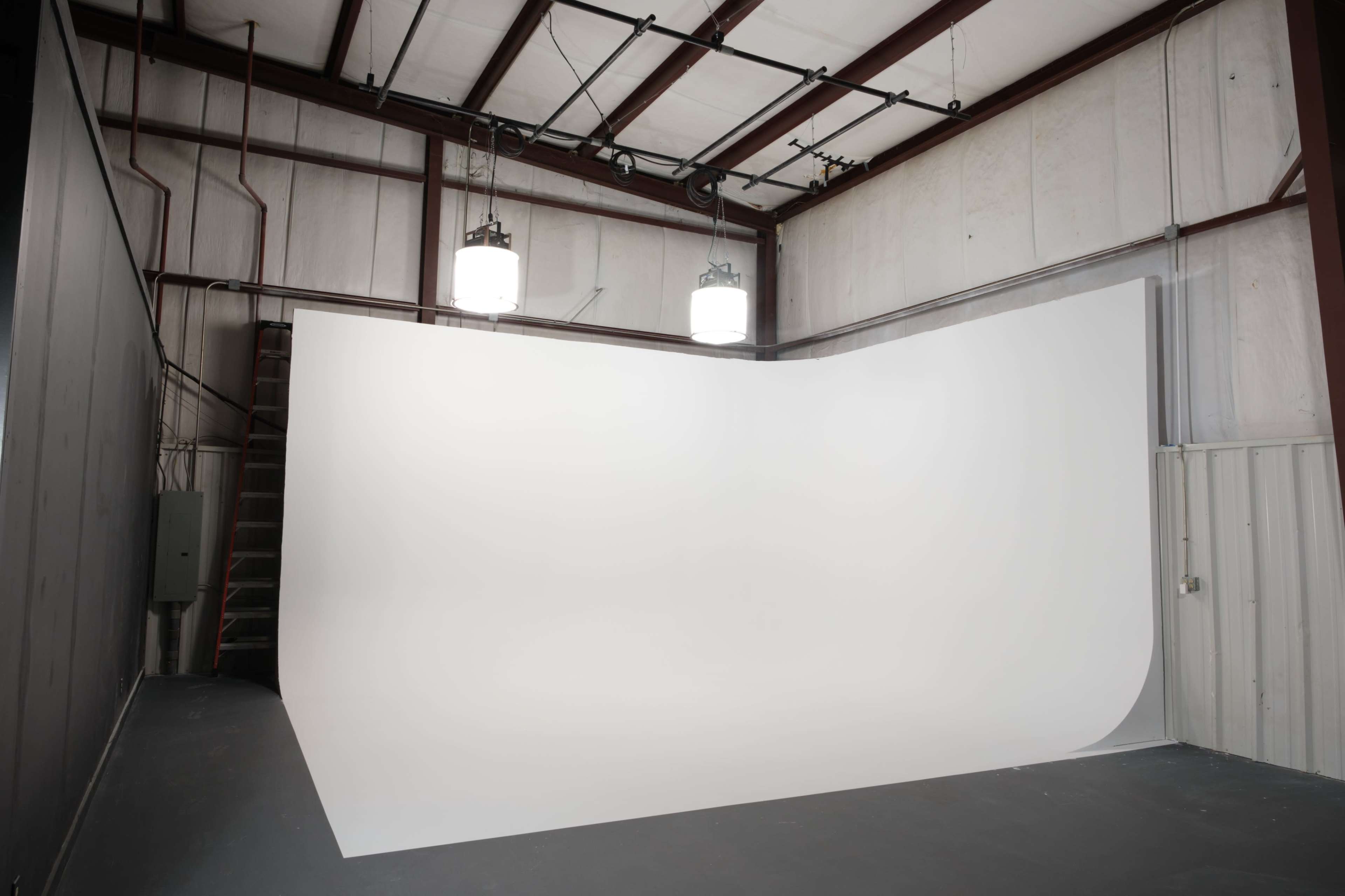 A spacious photography studio features a large, curved white backdrop and industrial lighting fixtures overhead.