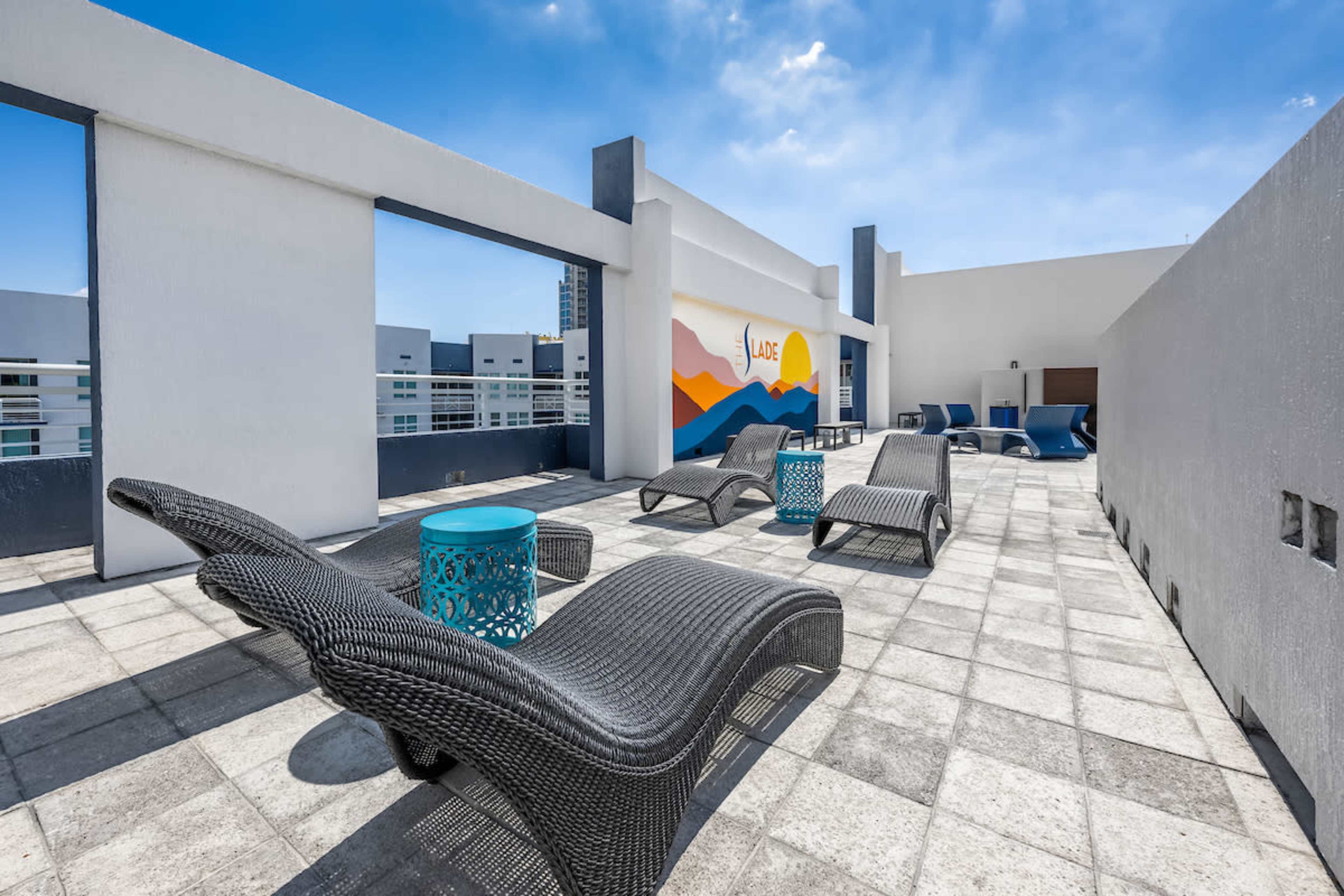 A rooftop terrace features several lounge chairs and tables under a clear blue sky.