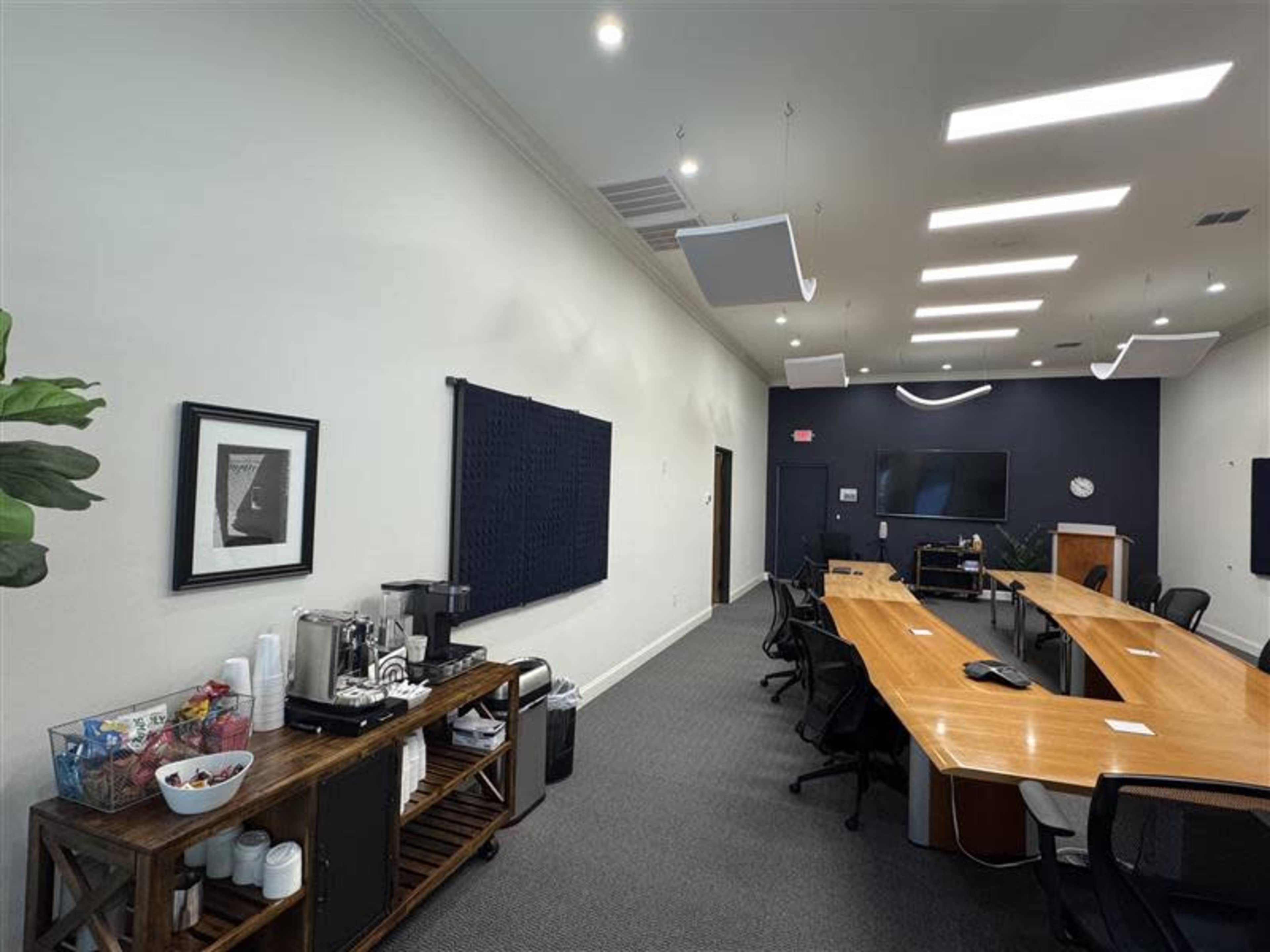 A conference room features a long wooden table with chairs, a coffee station, and a large screen at one end.
