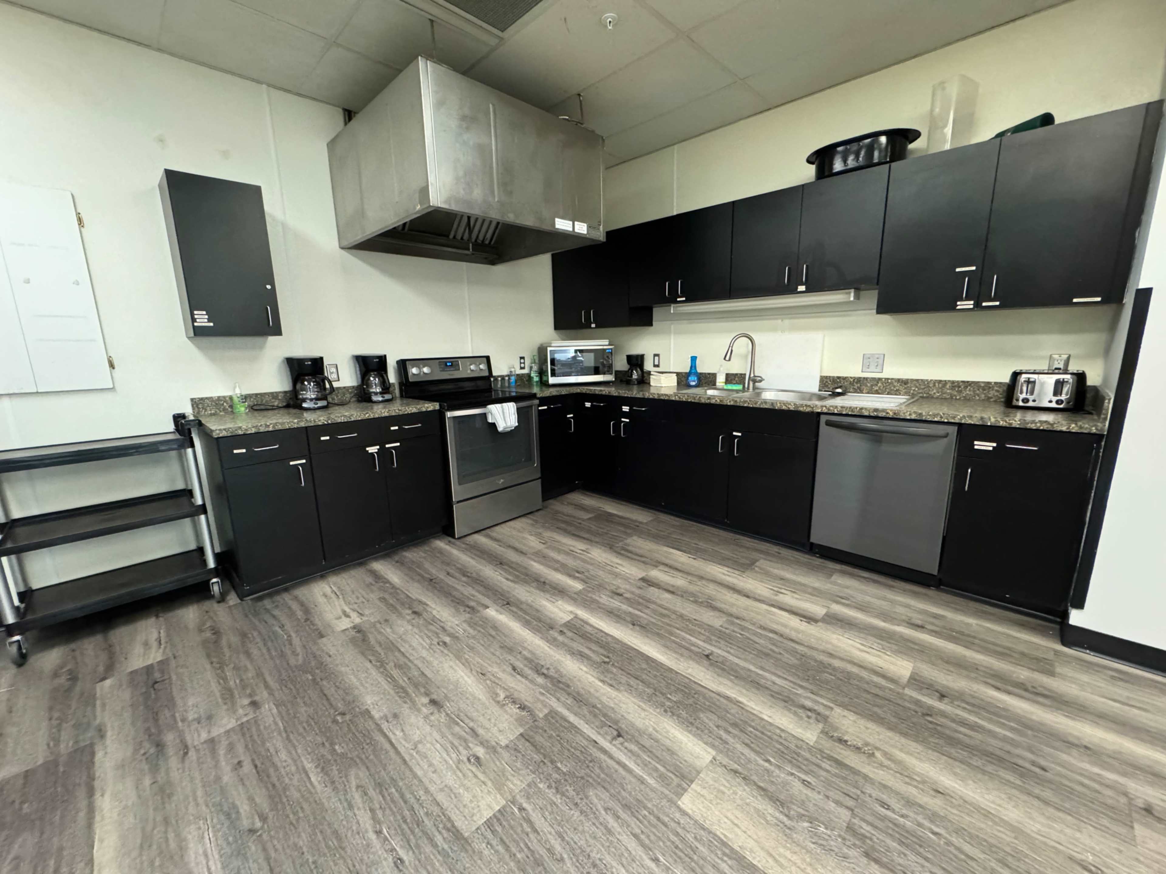 A modern kitchen with black cabinets, a stainless steel oven, a microwave, a sink, and a coffee maker on a countertop.