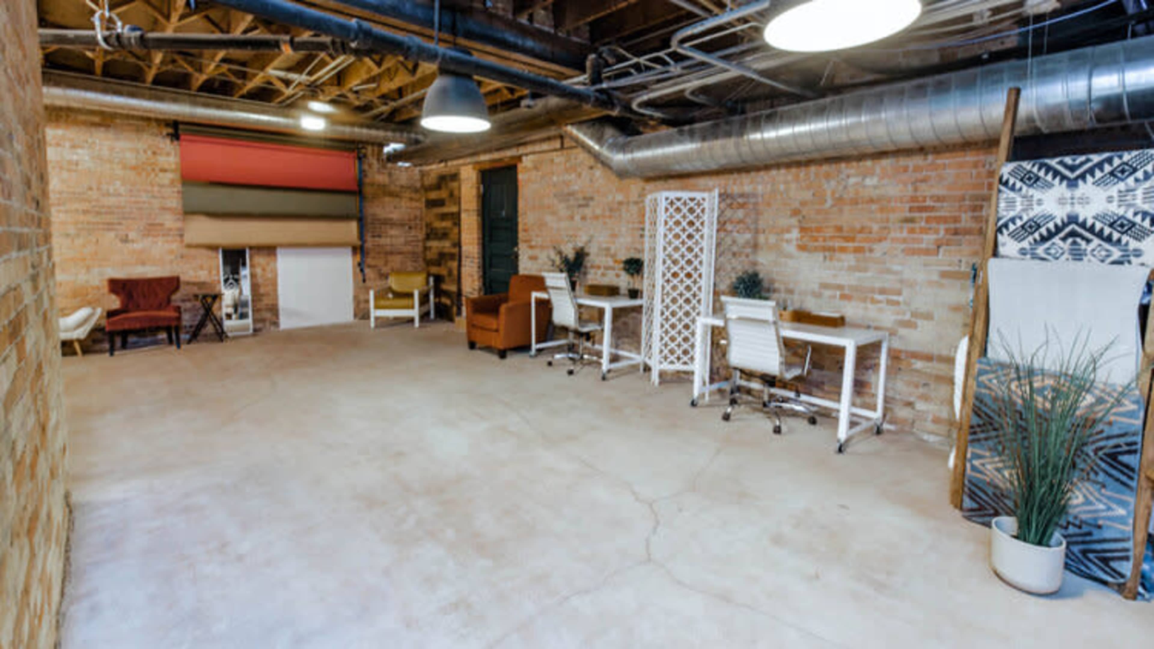 A spacious, industrial-style basement office with exposed brick walls, a concrete floor, and various seating arrangements and workstations.