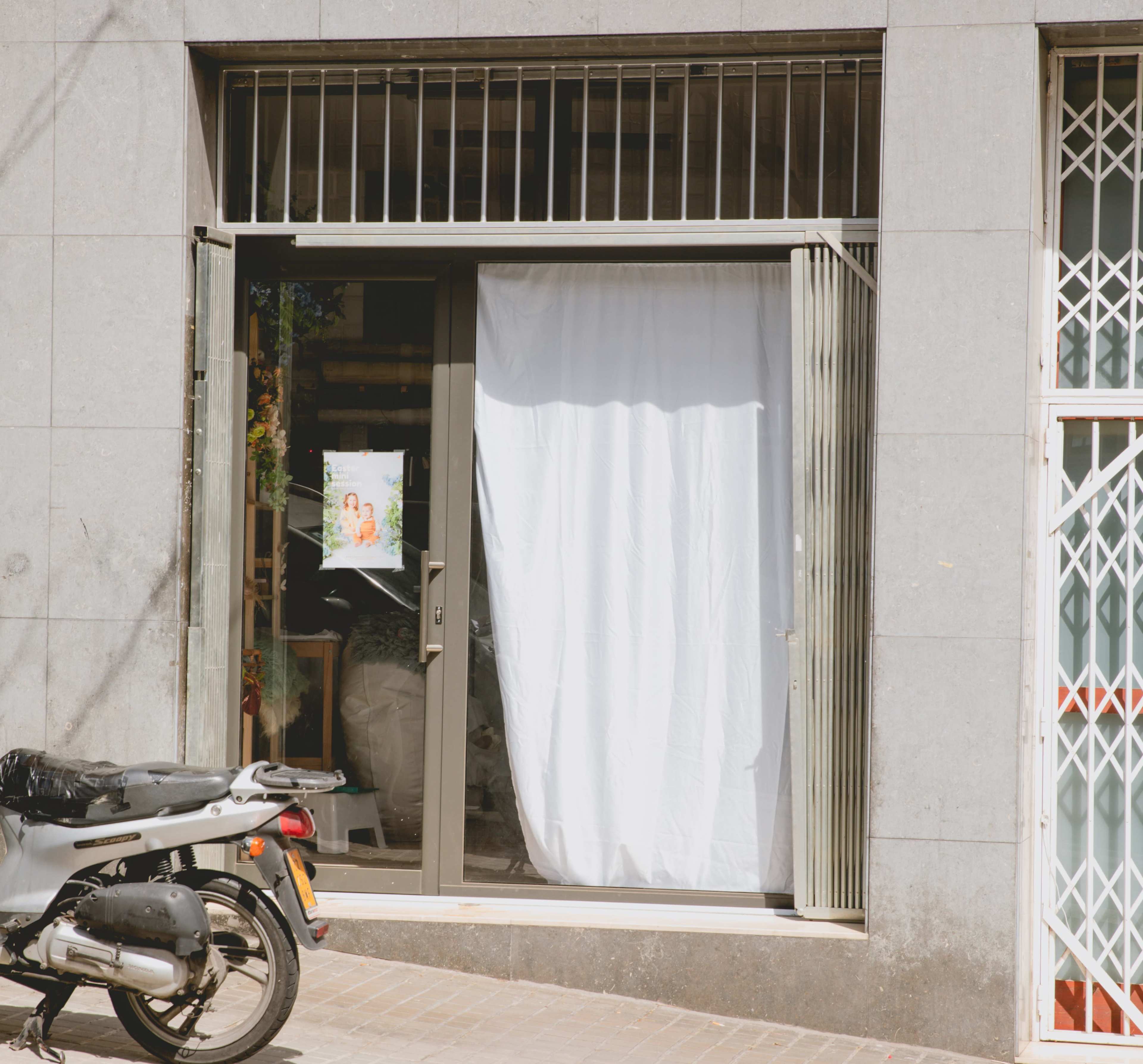 A storefront with a white curtain hanging in the doorway and a motorcycle parked outside.