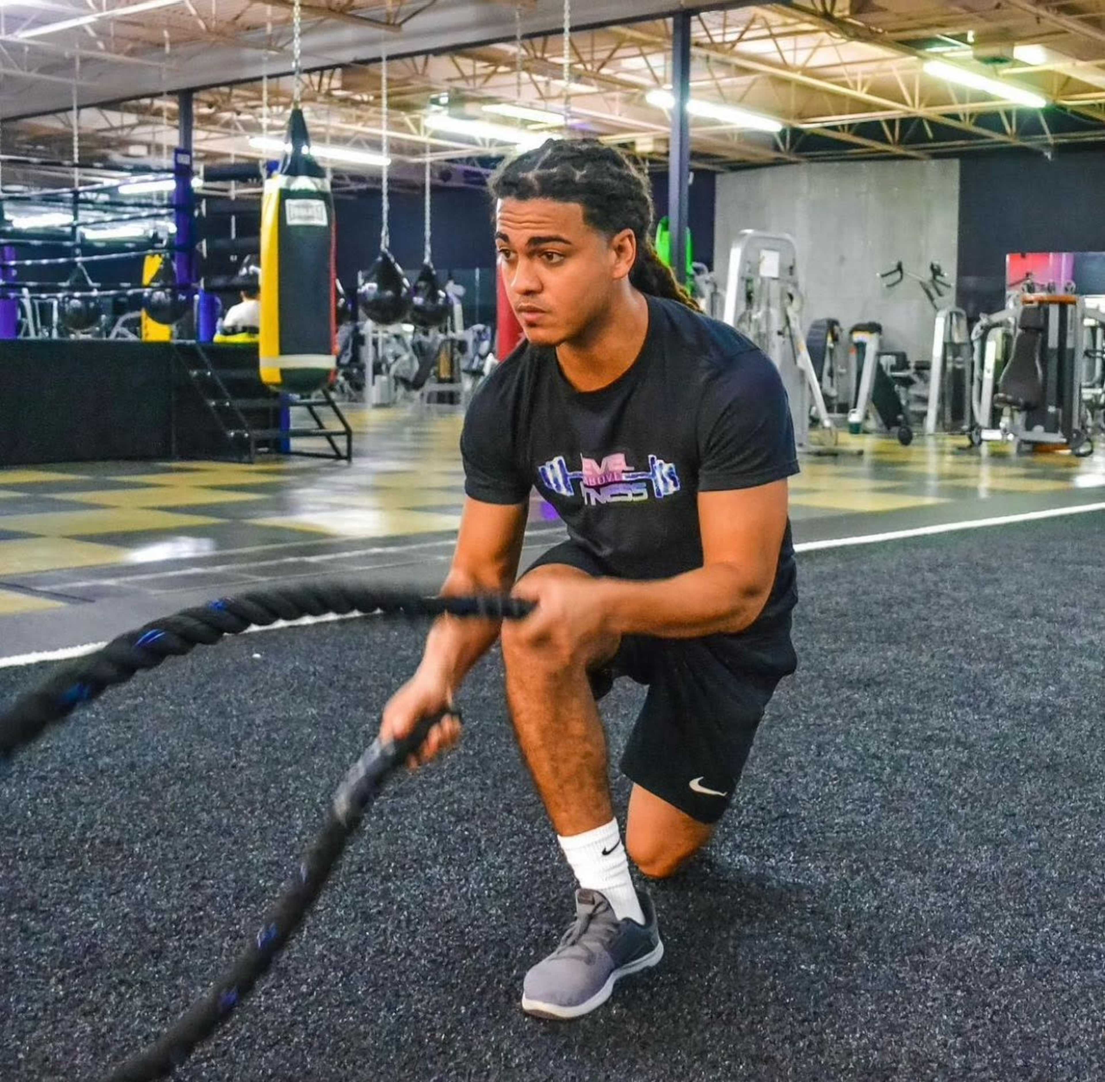 A person kneels on a gym floor while performing an exercise with battle ropes.