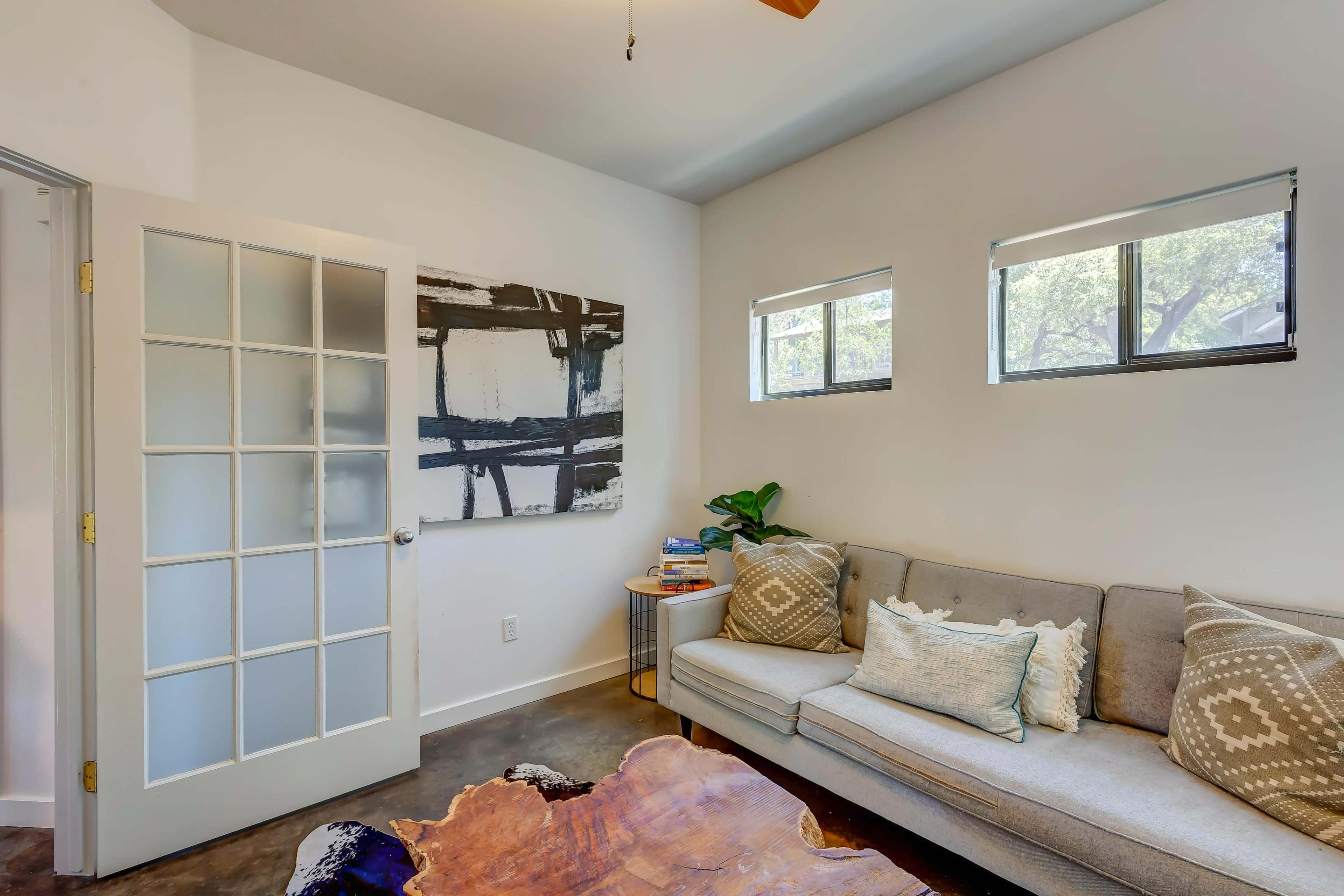A modern living room features a gray sofa with decorative pillows, a wooden coffee table, and a glass door leading to another space.