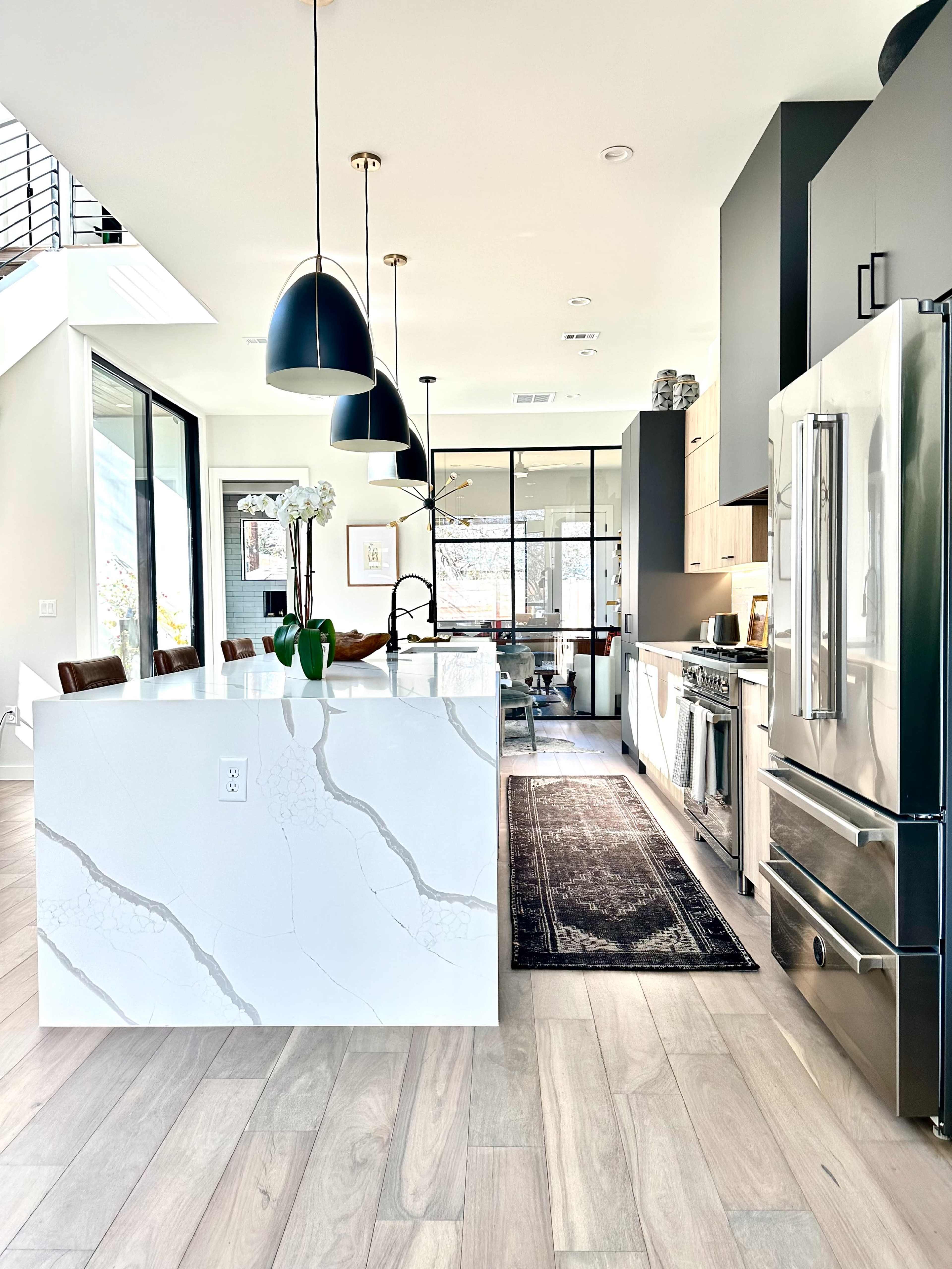 A modern kitchen features a large island with a marble countertop, sleek appliances, and pendant lighting above.