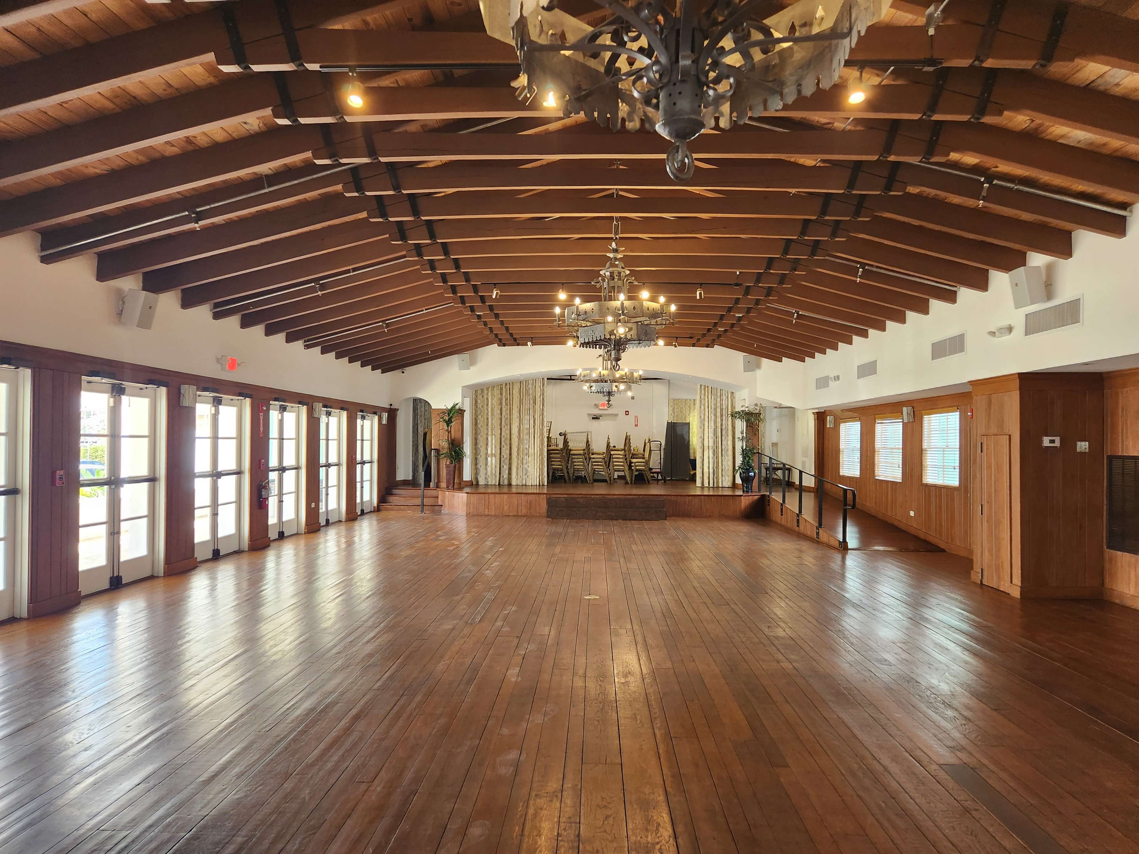 A spacious interior room with wooden floors, exposed beams, and a stage area at one end.