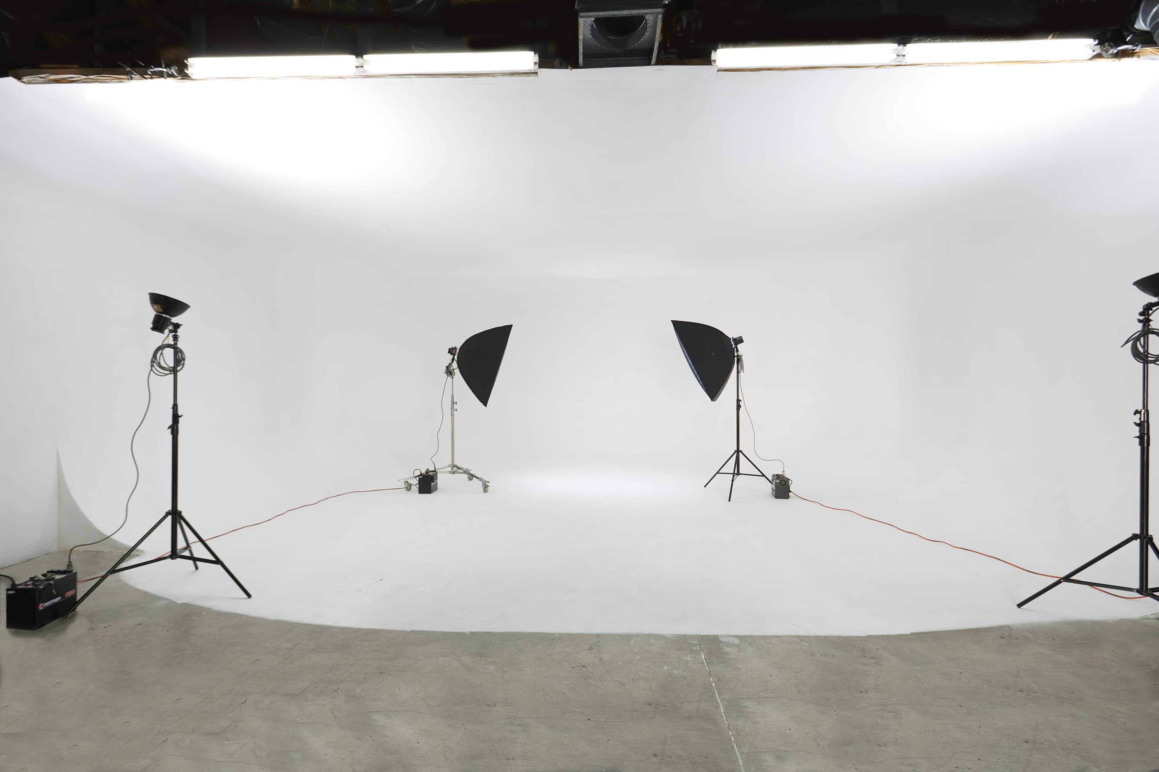 A photography studio with a white backdrop, three softbox lights, and a concrete floor.