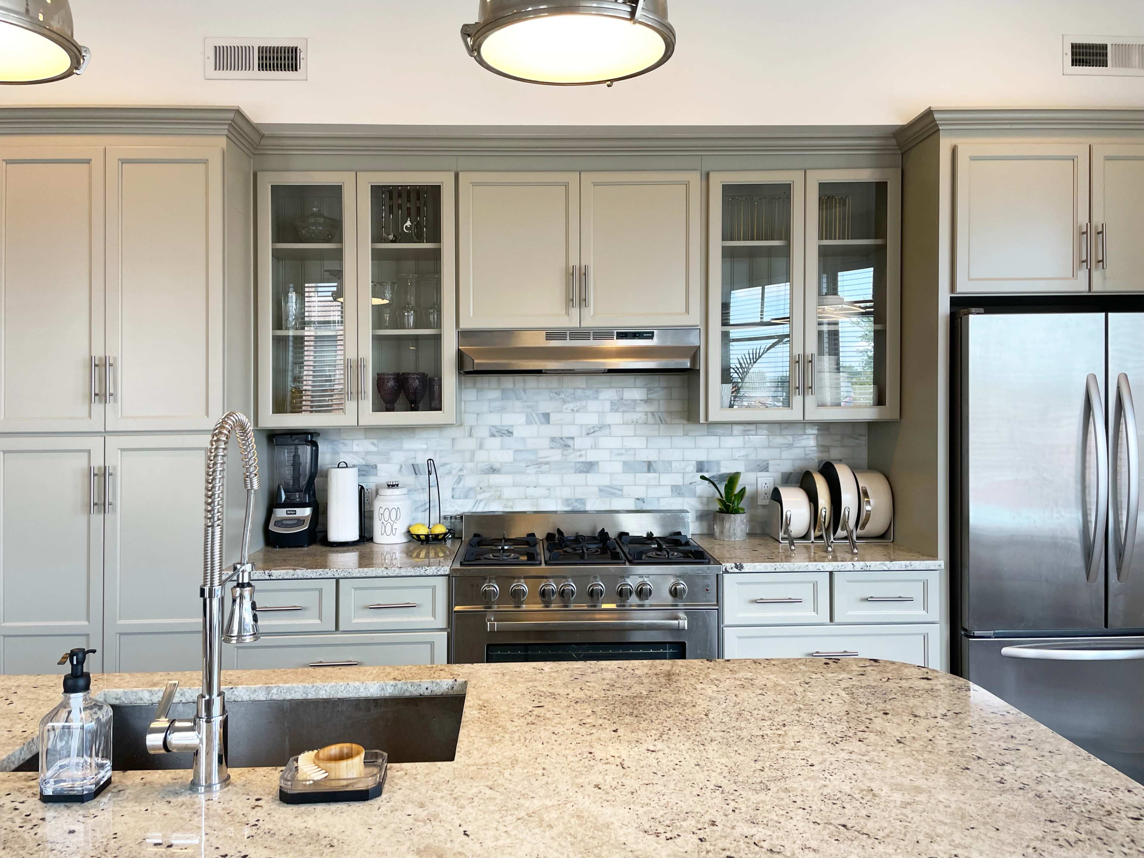 A modern kitchen features light cabinetry, a marble backsplash, stainless steel appliances, and a large island with a sink.