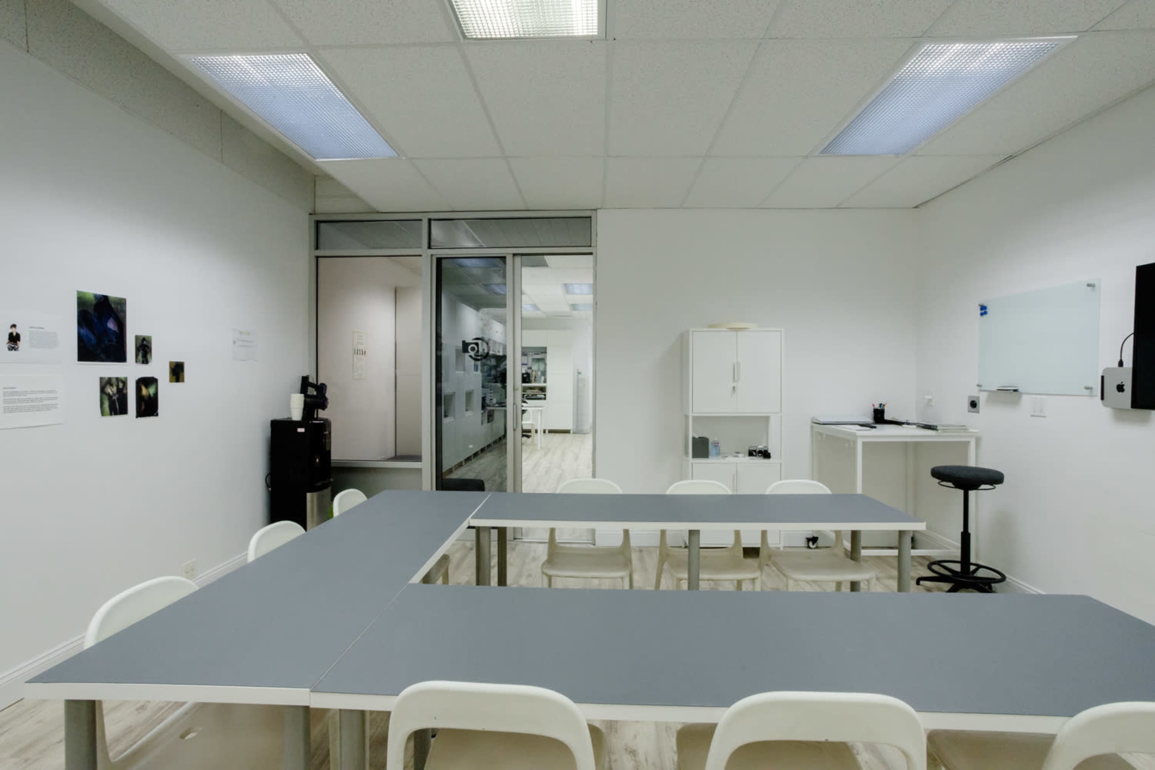 The image shows a simple classroom setting with a gray rectangular table and white chairs arranged around it, flanked by walls that have minimal decorations.