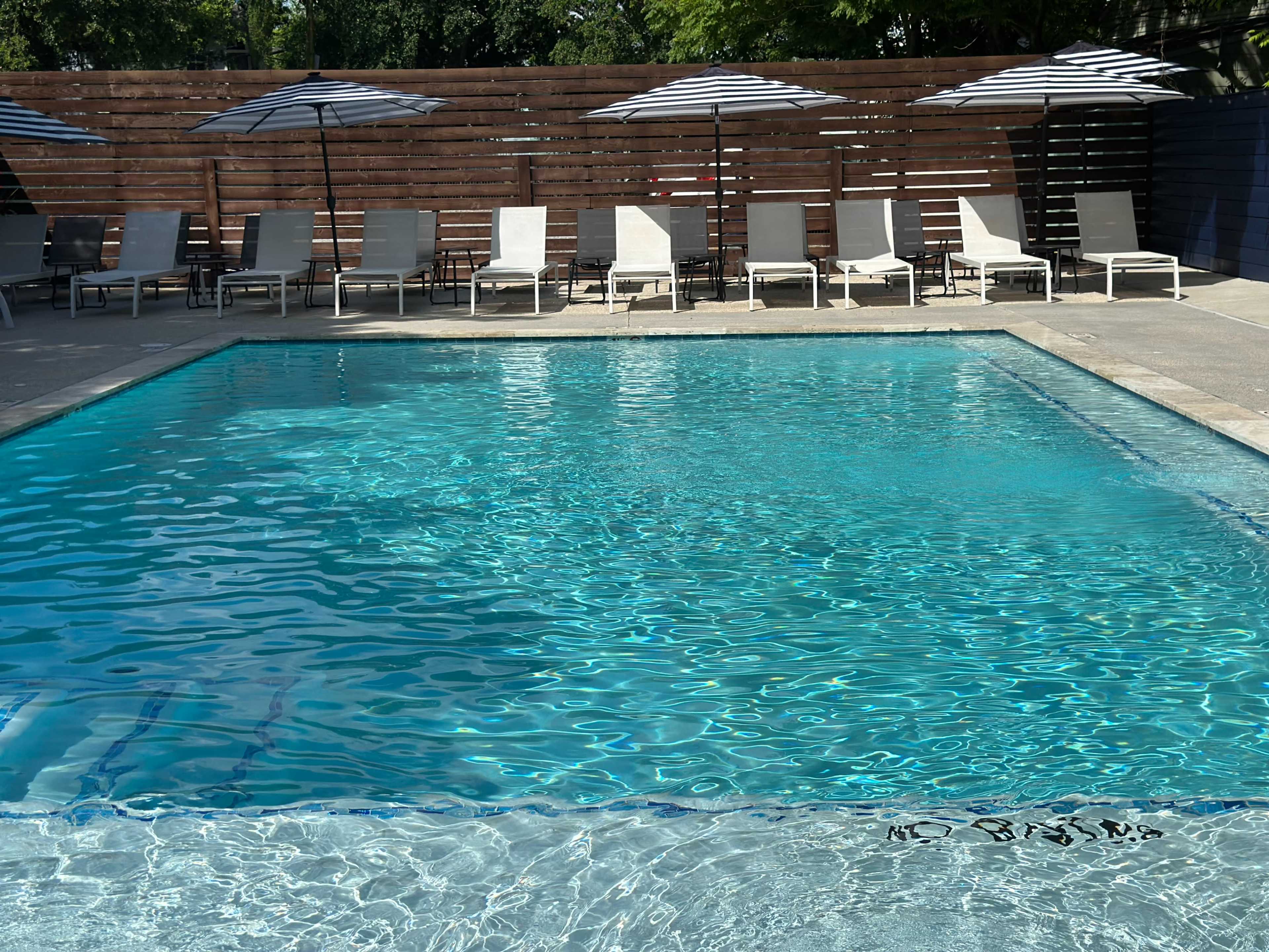 The image shows a swimming pool surrounded by sun loungers and umbrella shades.