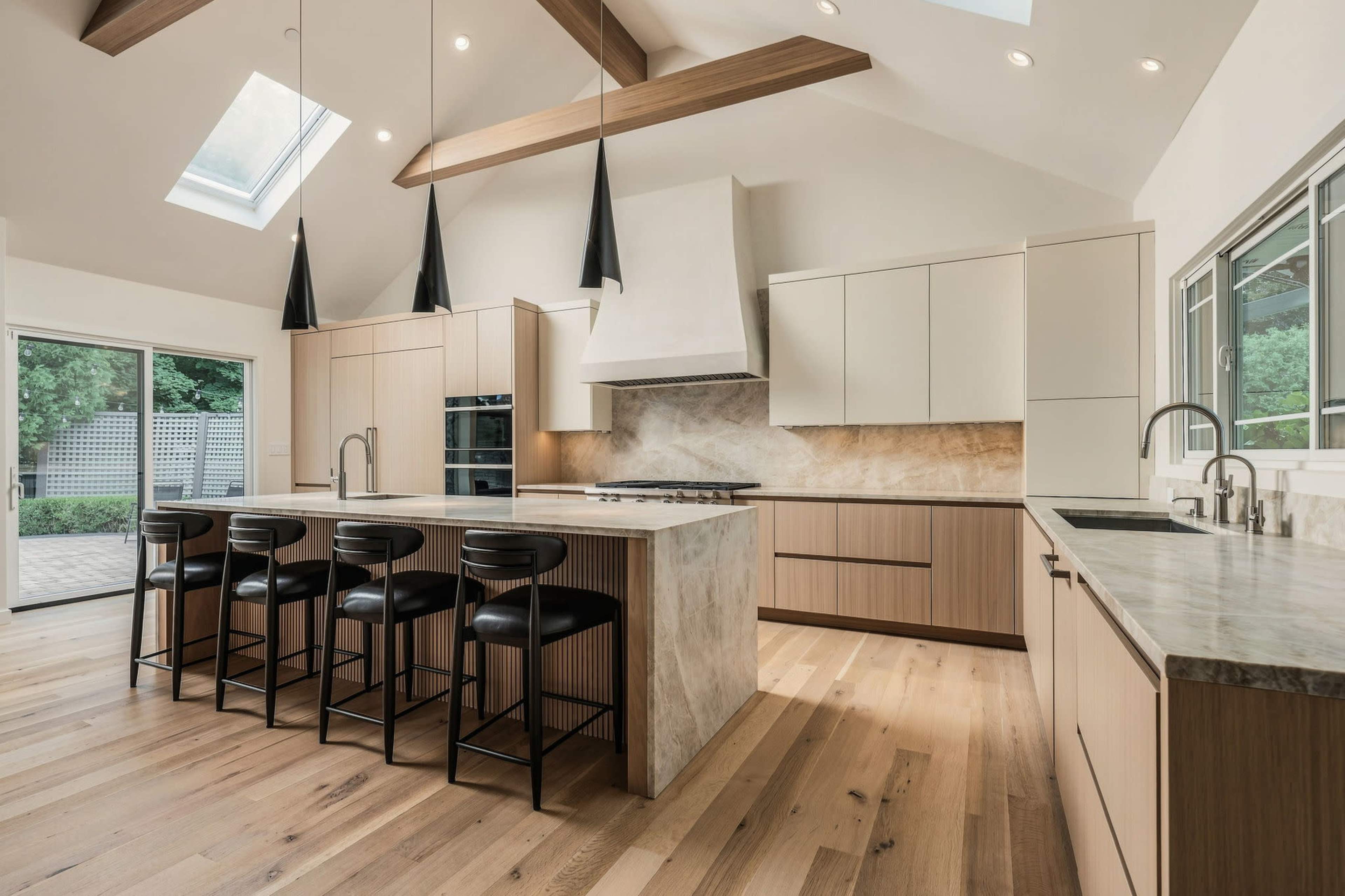 The image showcases a modern kitchen featuring a spacious island with seating, sleek cabinetry, and large windows that allow natural light to fill the room.