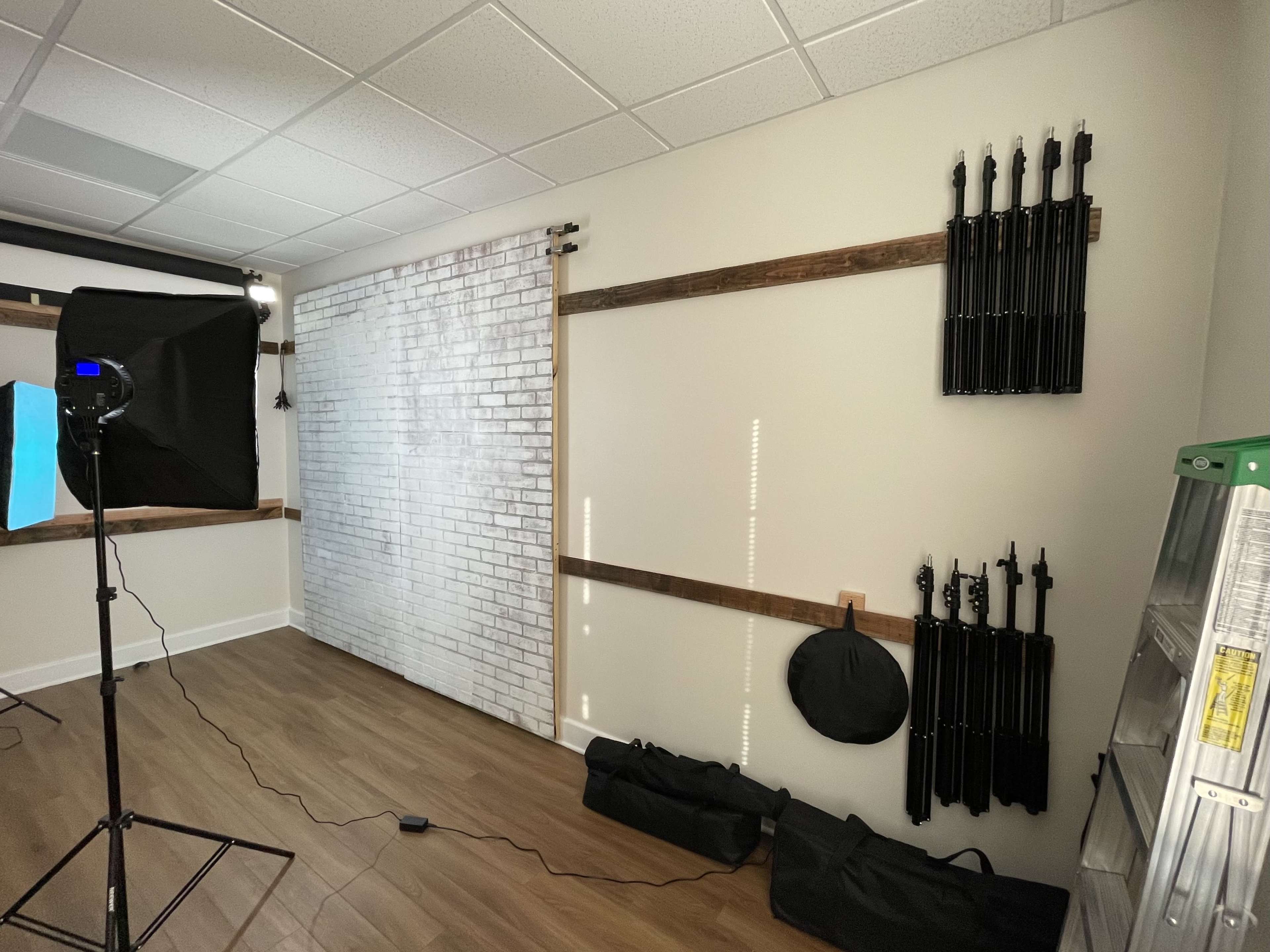 A photography studio with a white brick wall, a light umbrella, and various equipment neatly stored on a wooden wall.
