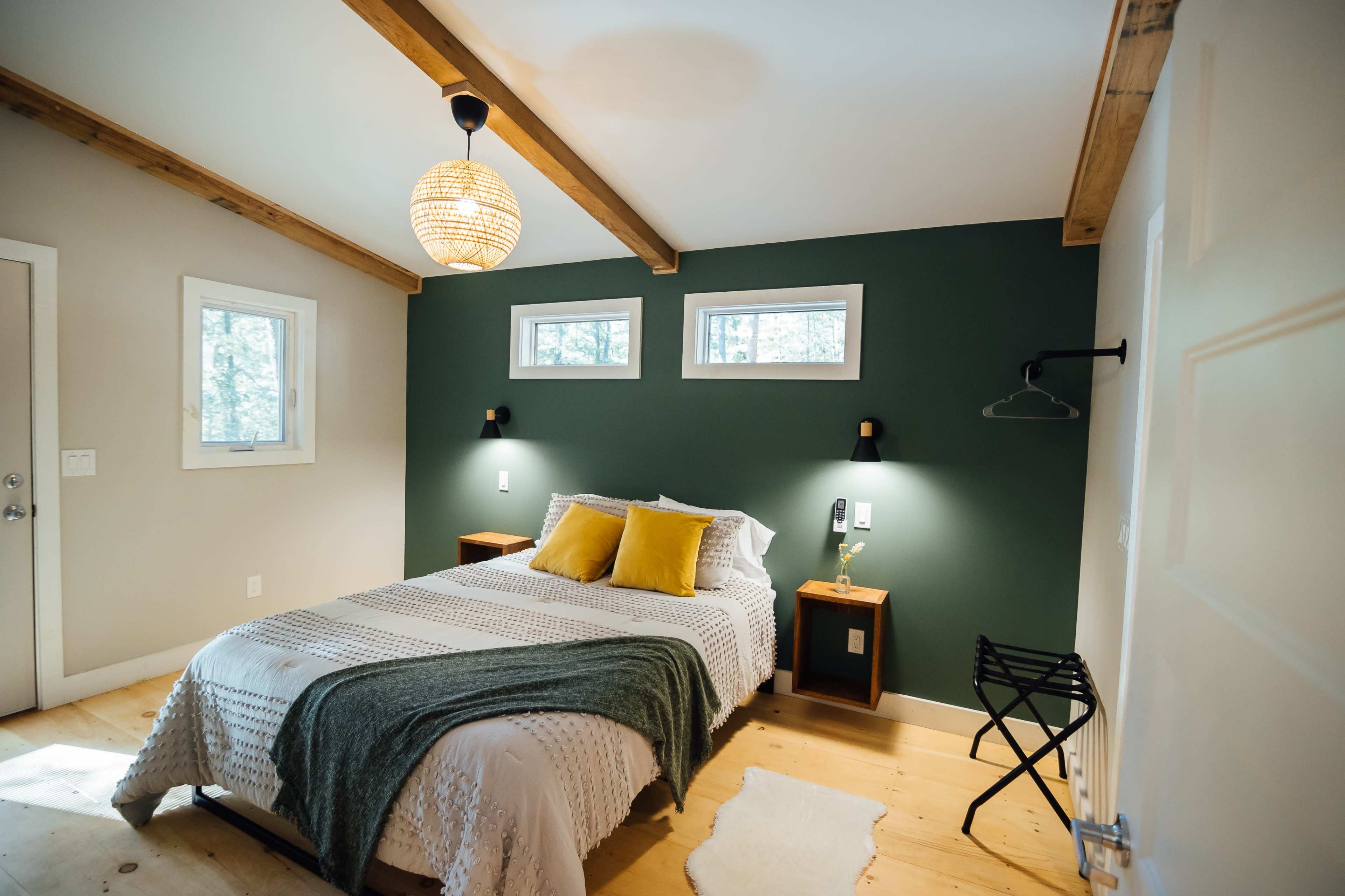 A cozy bedroom featuring a bed with a patterned blanket and yellow pillows, wooden beams on the ceiling, and two small bedside tables with lamps.