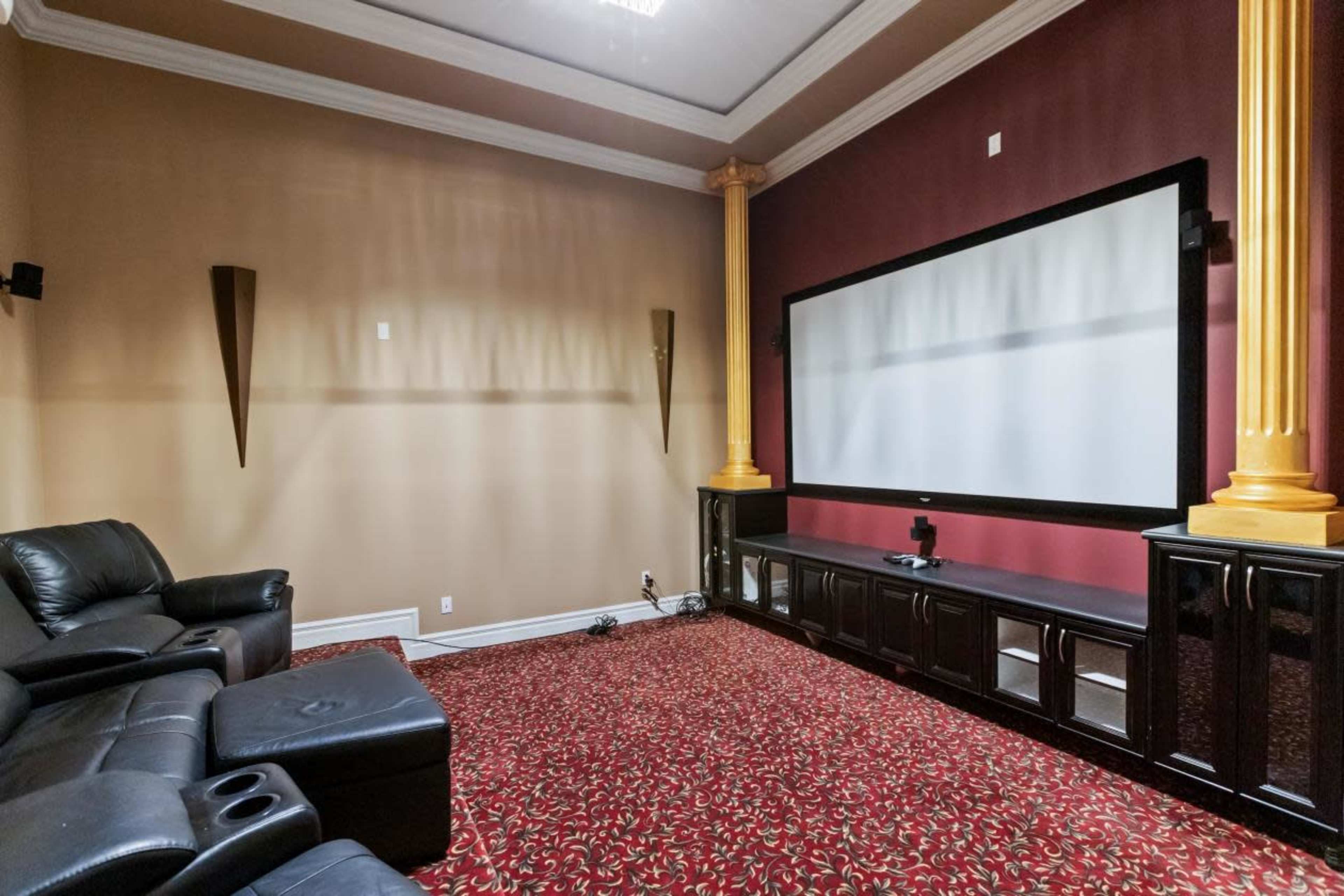 A home theater room with dark leather seating, a large flat-screen display, and decorative columns on the walls.