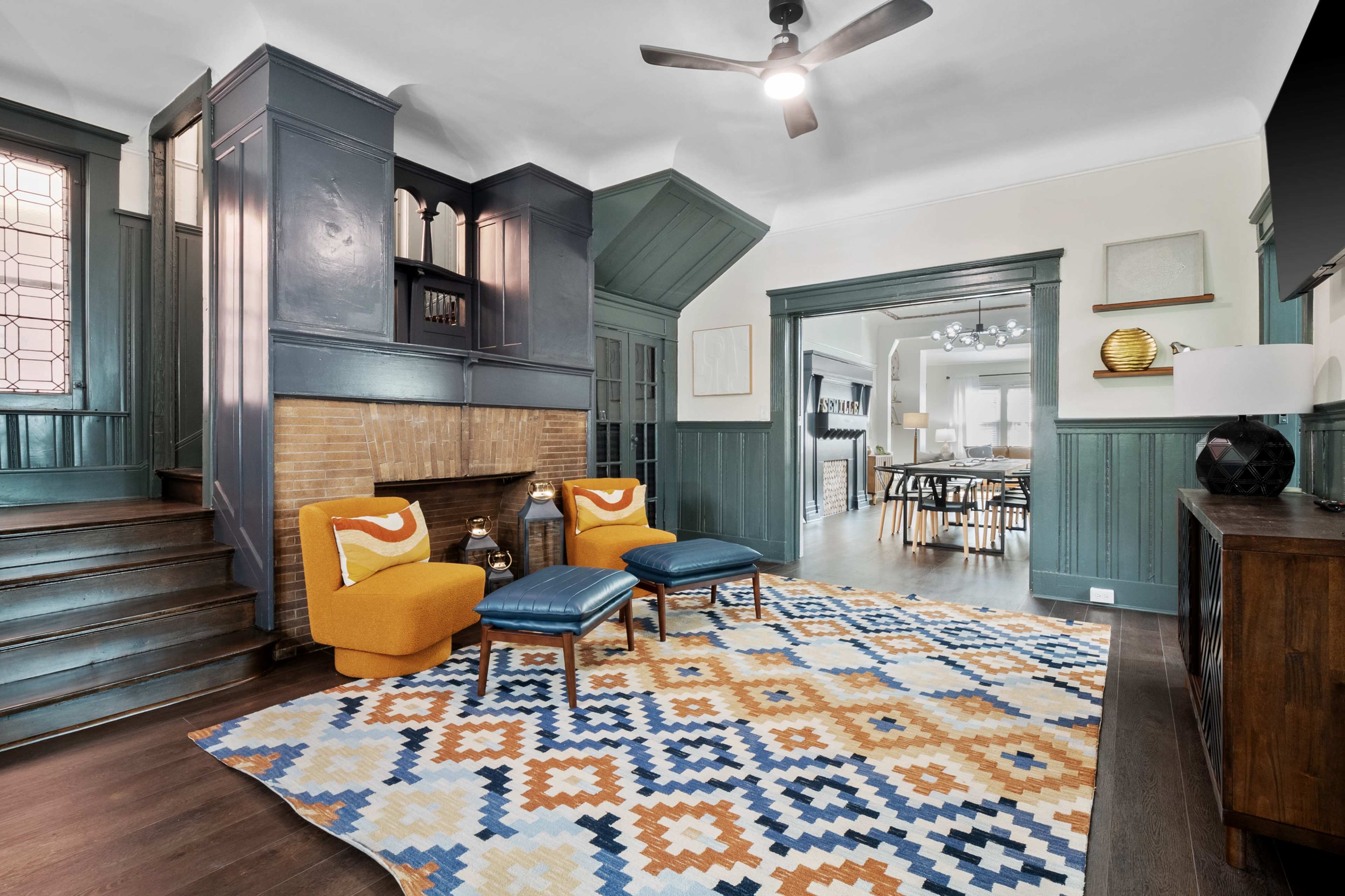 A stylish living room featuring a blue and orange color scheme, with two armchairs, a patterned area rug, and a fireplace surrounded by wooden paneling.