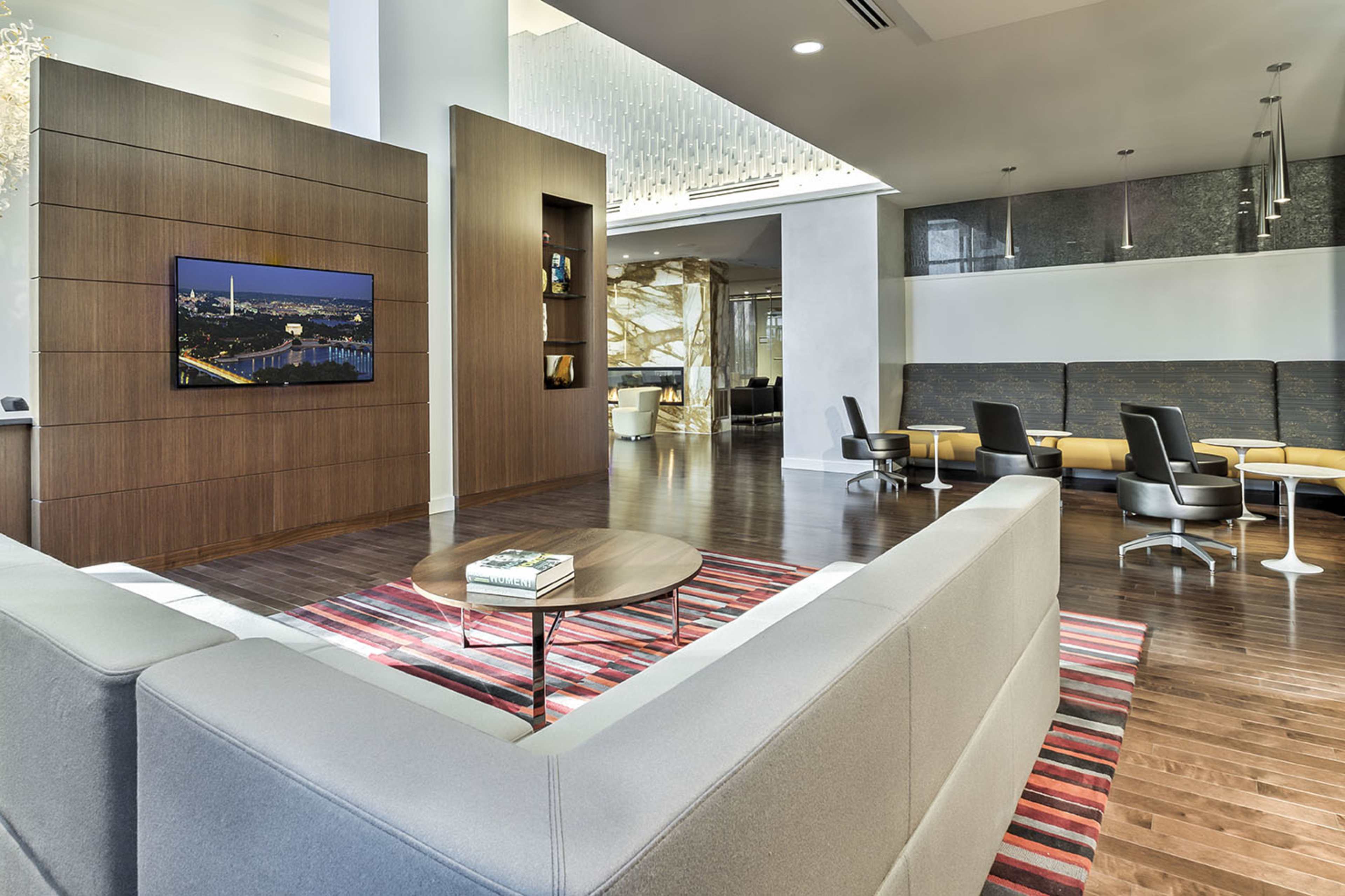 A modern lounge area featuring a gray sofa, a wooden wall-mounted television, and stylish seating arrangements on a hardwood floor.