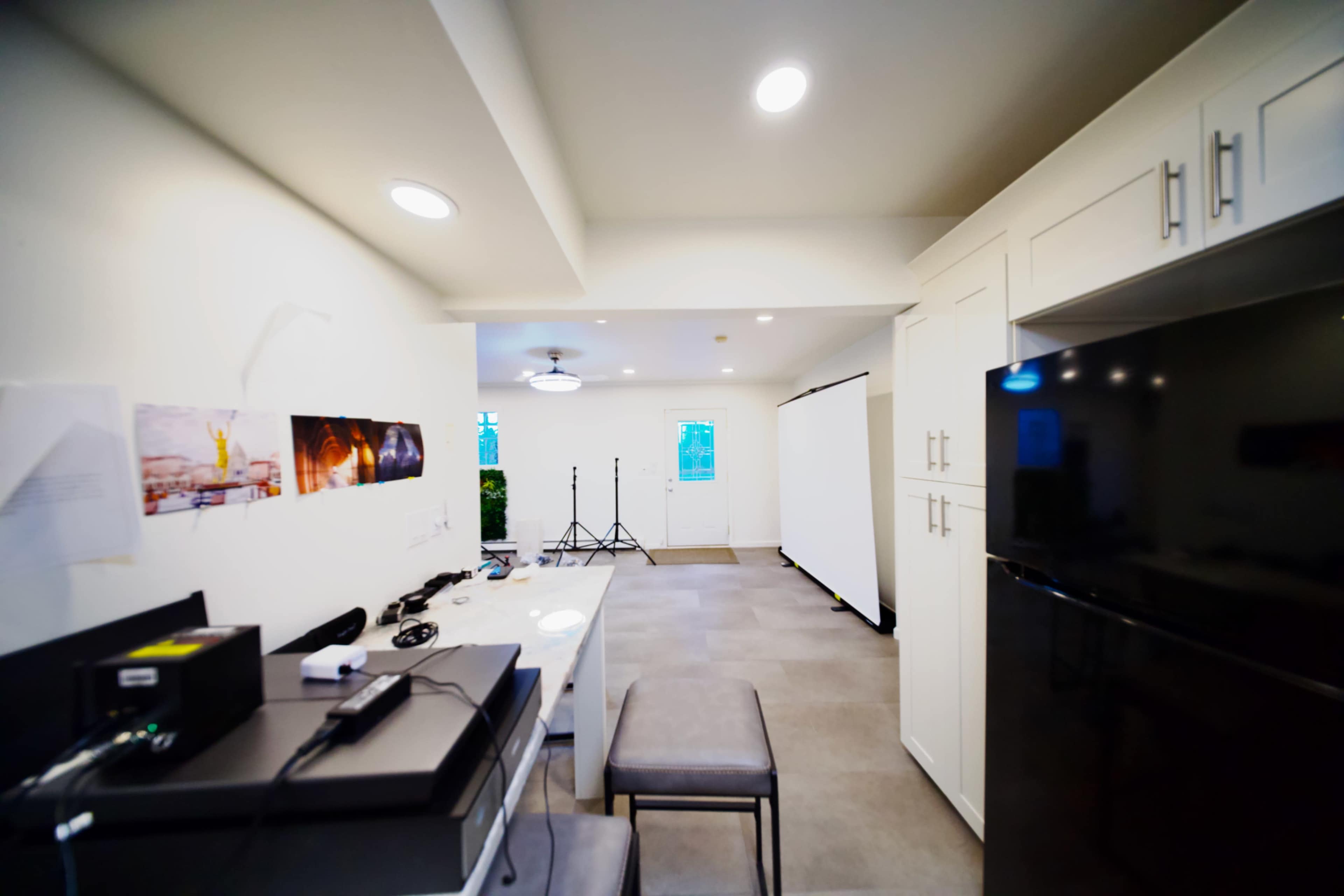 The image shows a modern, sparsely furnished room with a kitchen area on one side and a space for photography equipment on the other.