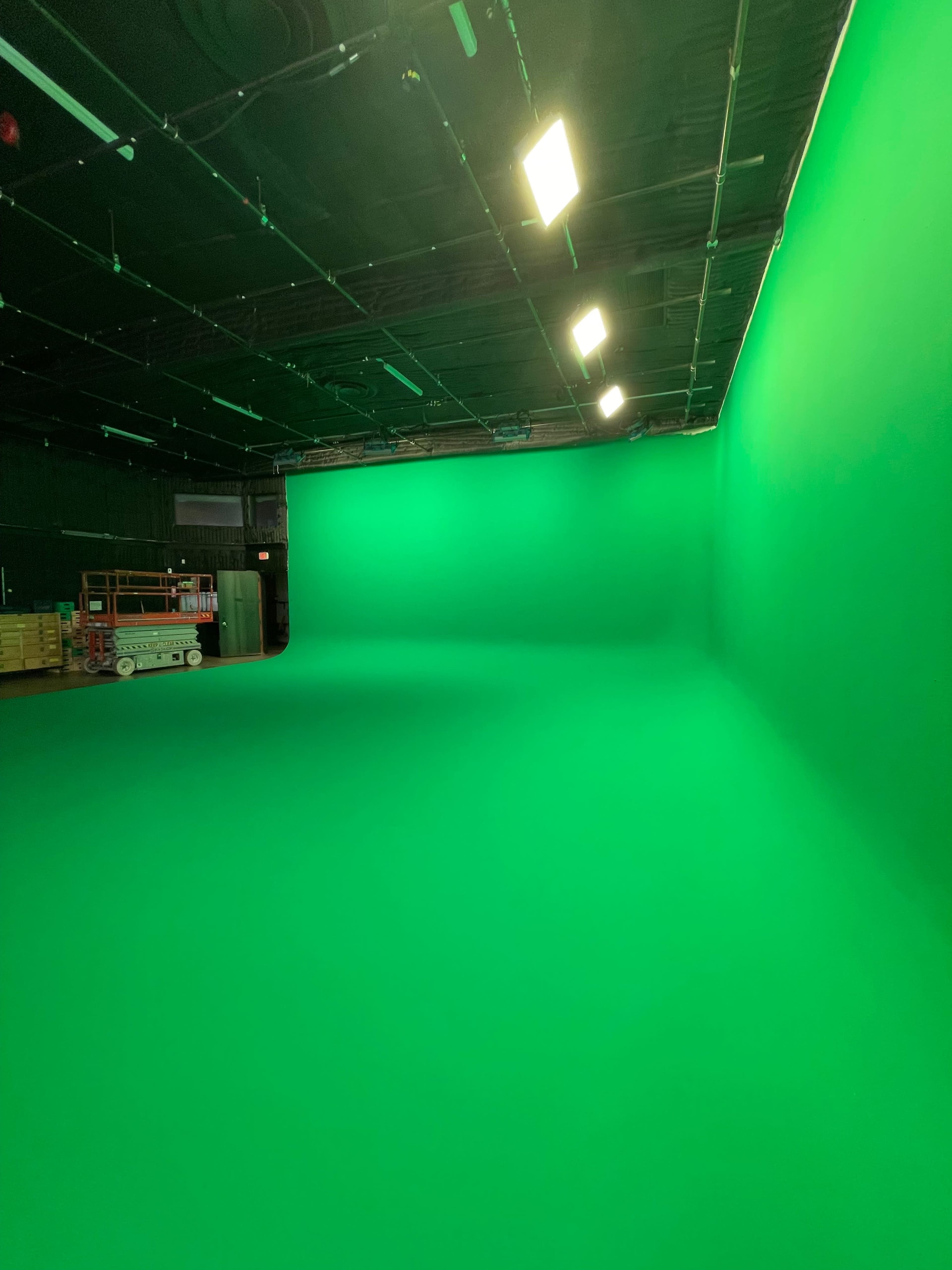 An empty studio featuring a large green backdrop with overhead lights.
