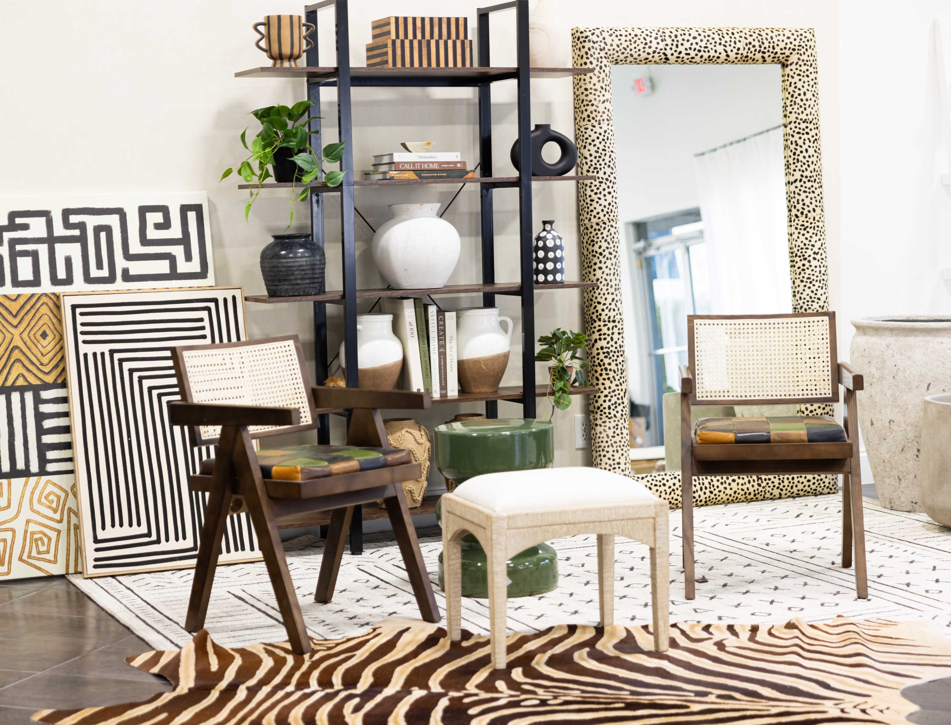 The image features a modern interior decor setting with two patterned chairs, a small white stool, a wooden bookshelf displaying decorative items, and an animal-print rug on a dark floor.