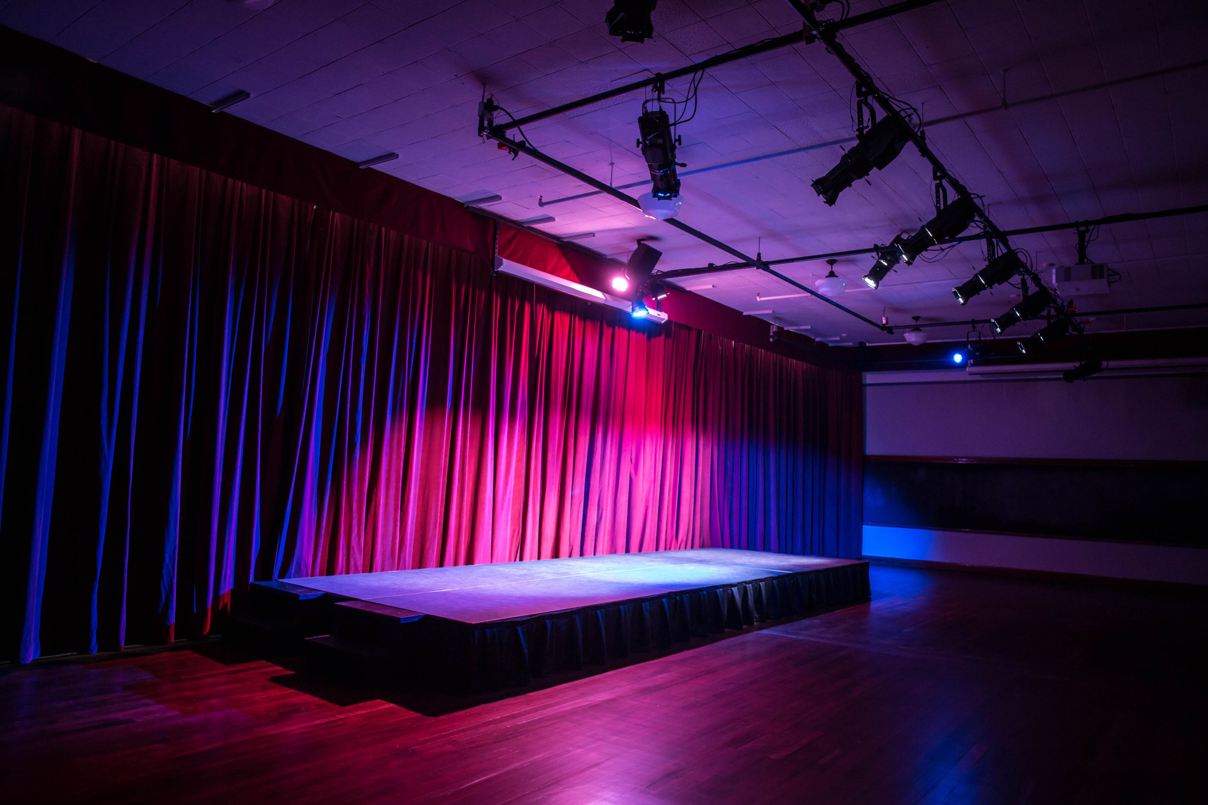 An empty stage with a raised platform and colorful curtains in a dimly lit room.