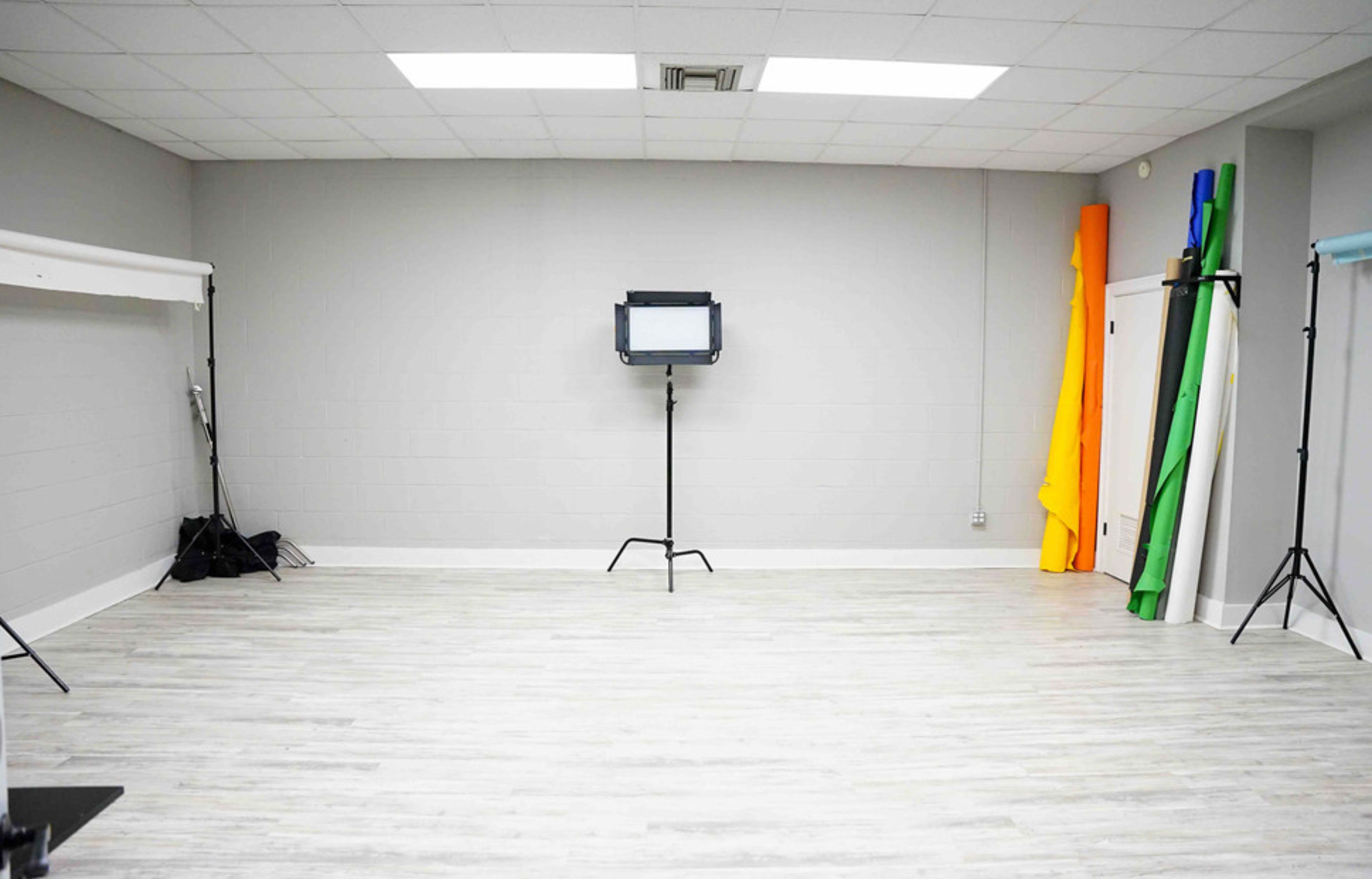 A spacious studio with gray walls, a light-colored floor, and various colored backdrops leaning against the wall.