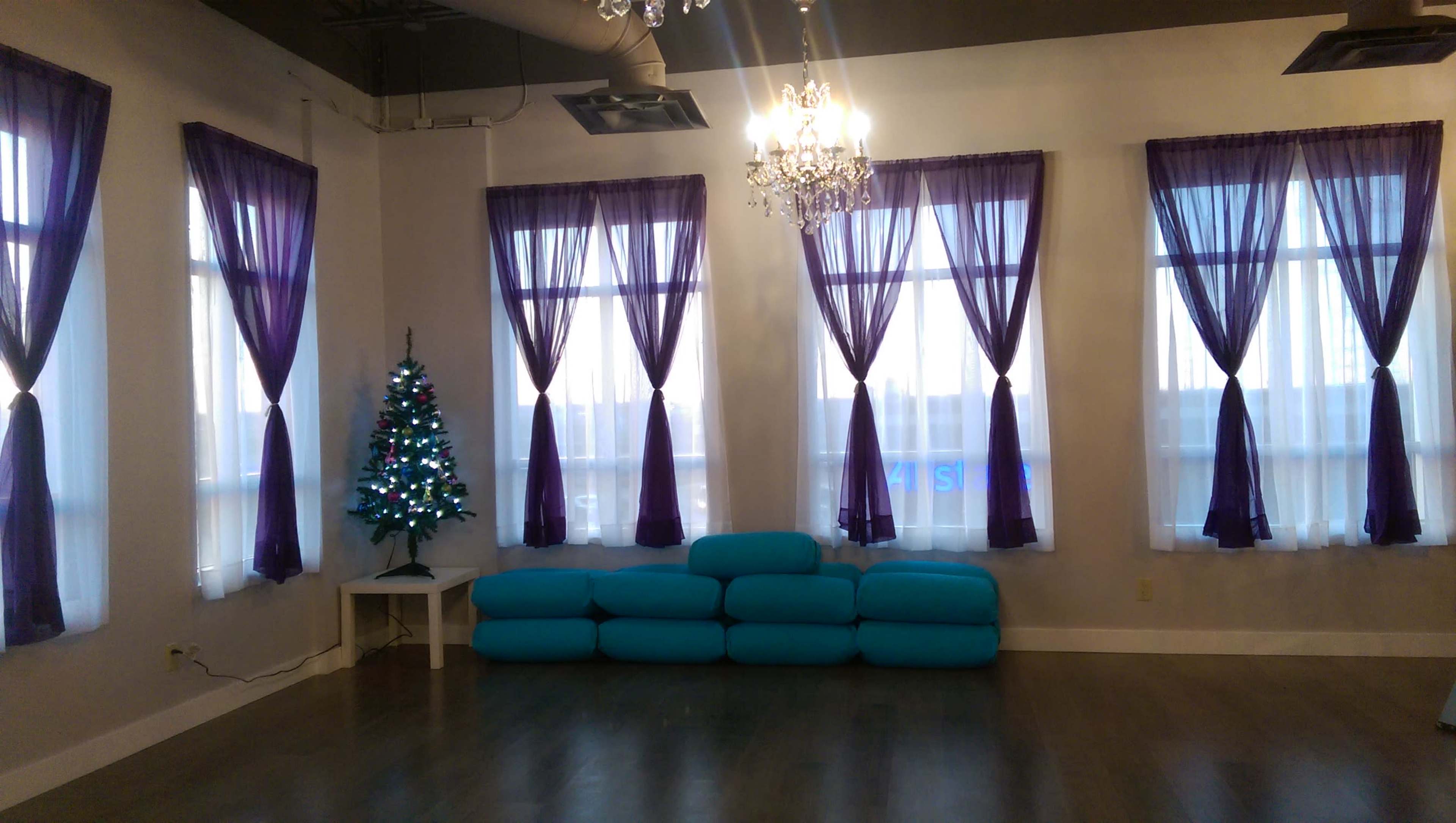 A spacious room with purple curtains, a small decorated Christmas tree, and a teal seating area against the wall.