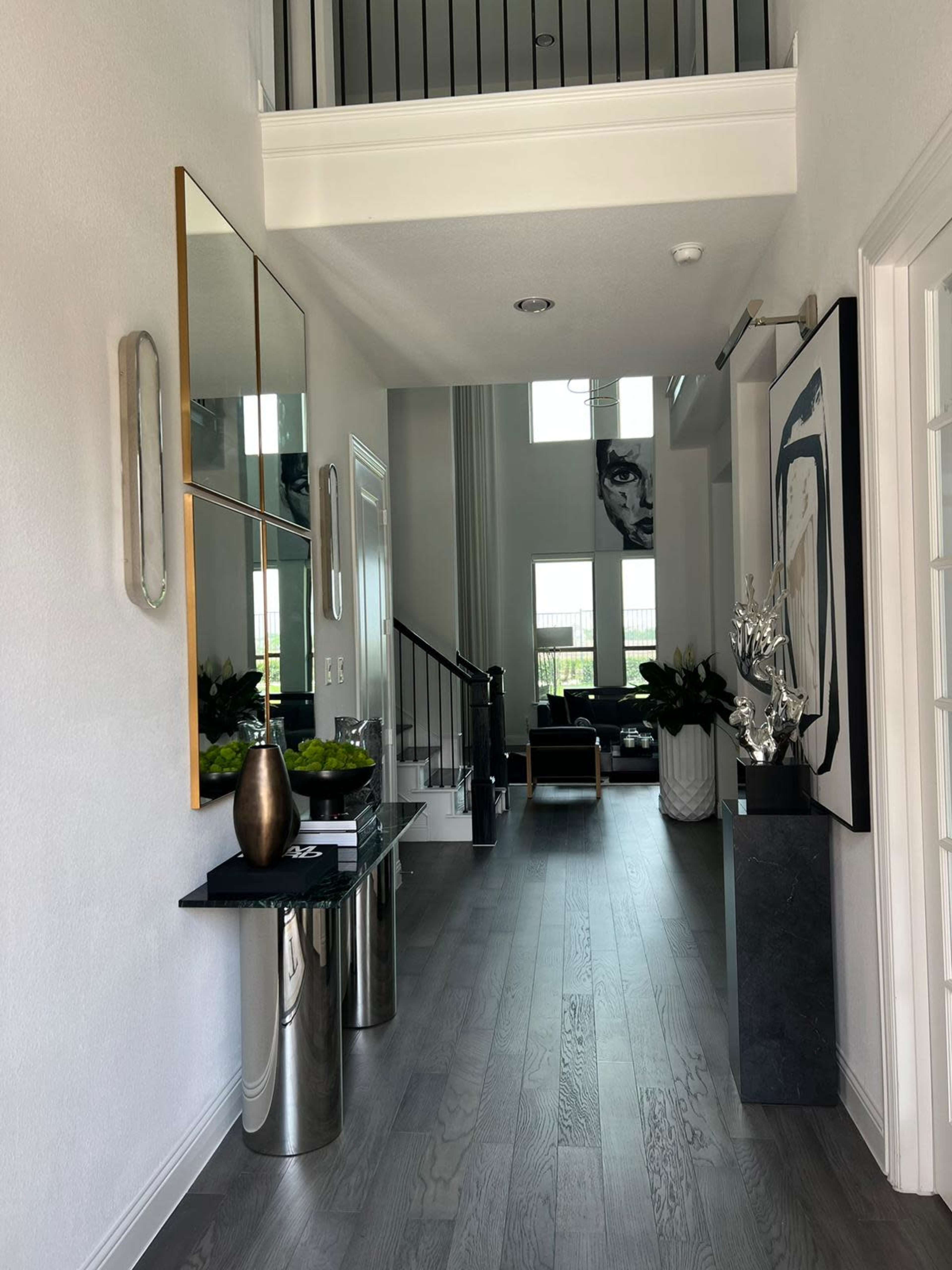 A modern hallway features a console table with a mirror, decorative items, and a view of a living area with large windows.