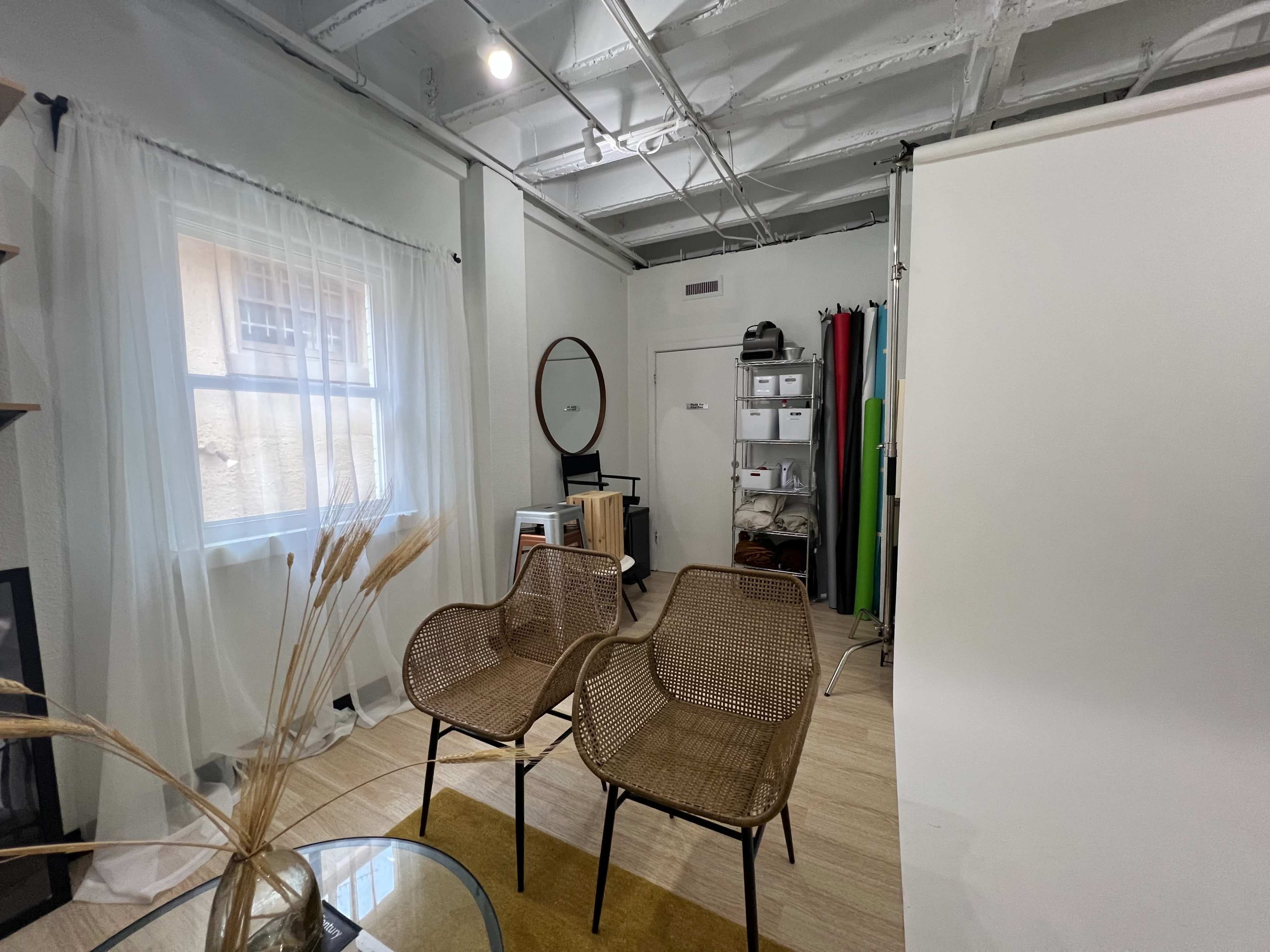 A bright room featuring two wicker chairs, a round mirror, and a shelving unit with various storage bins against a backdrop of colorful fabrics.